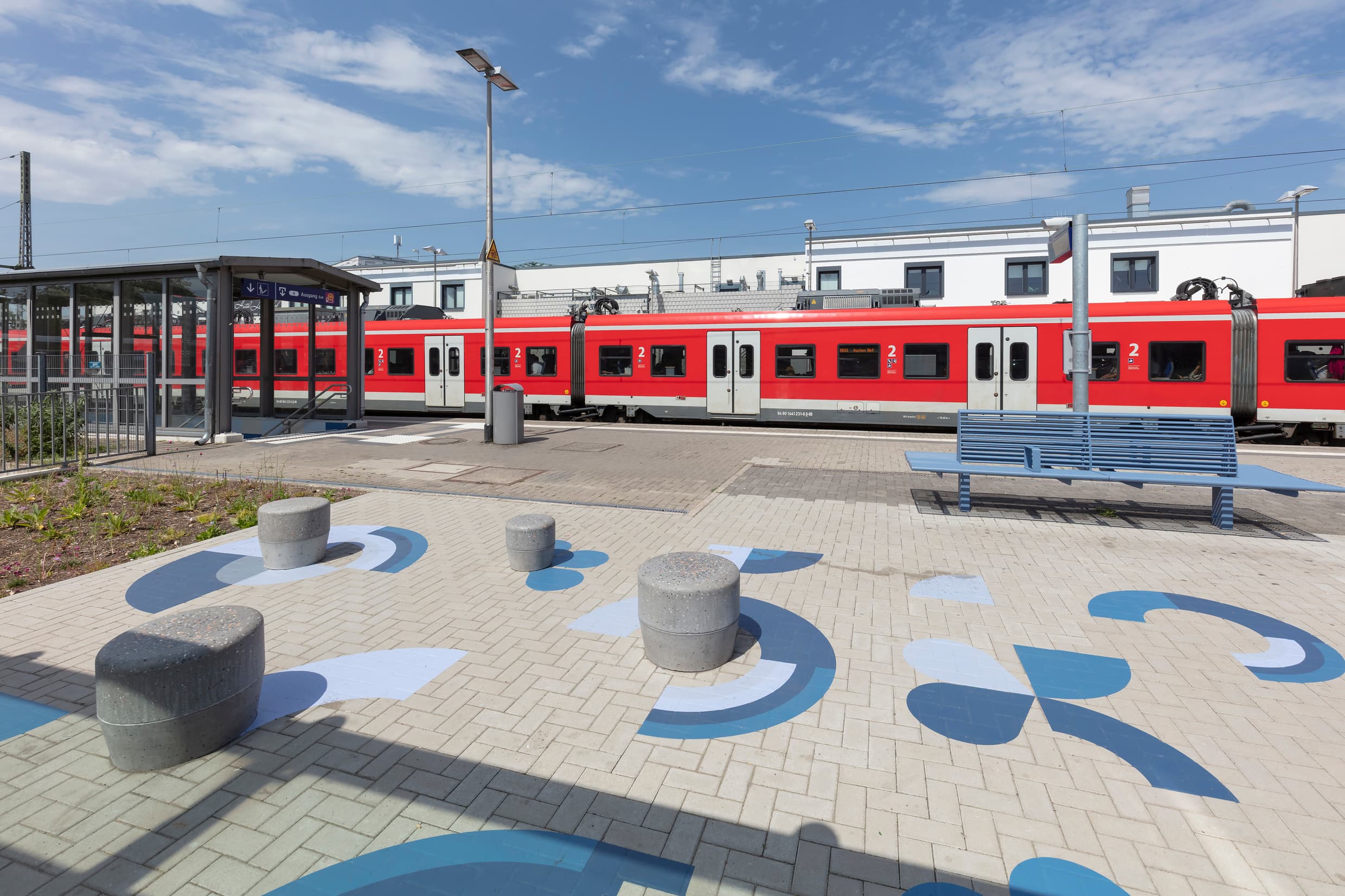 Moderne Betonhocker am Bahnsteig mit Bodenbemalung.