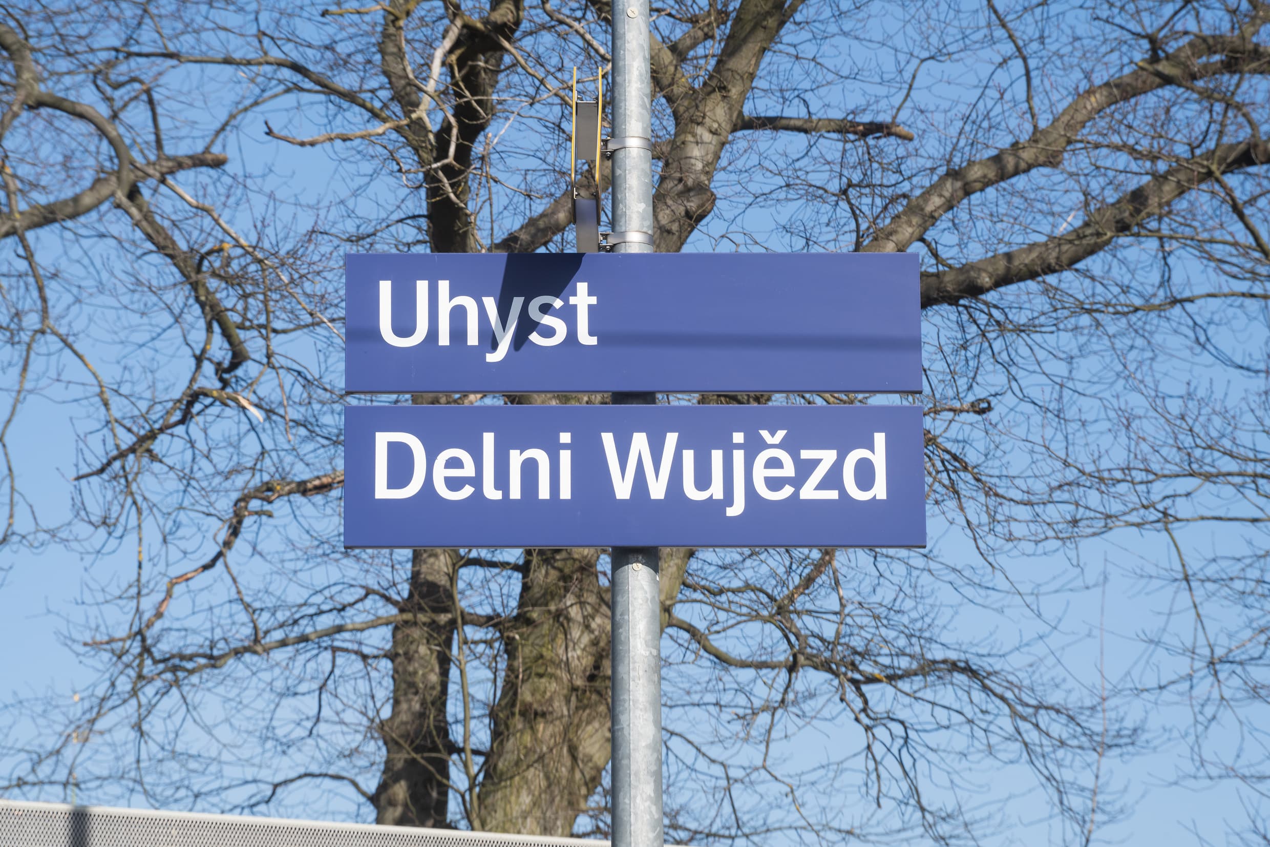 Zwei blaue Schilder, die untereinander angeordnet sind und den Bahnhofsnamen zweisprachig abbilden. Uhyst auf deutsch und Delni Wujezd auf sorbisch. 