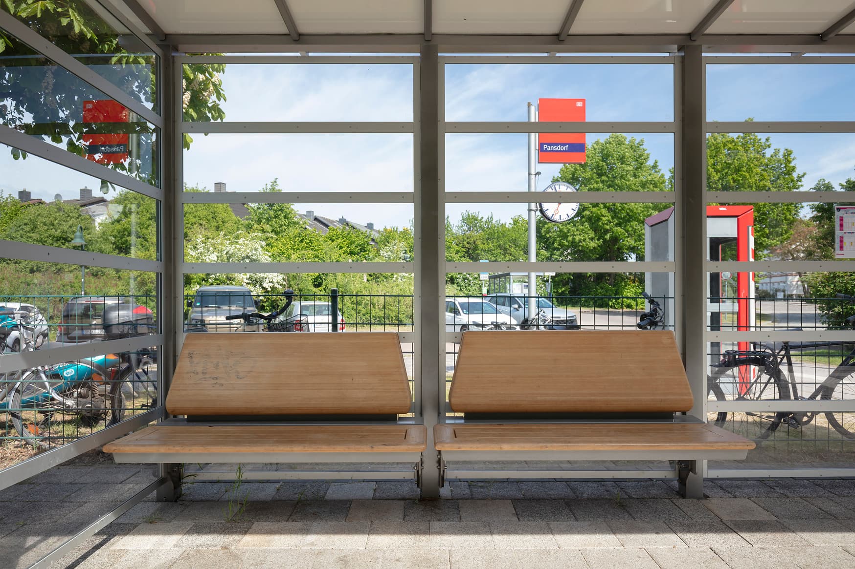 Sitzbänke in Holzoptik im transparenten Wetterschutzhäuschen.
