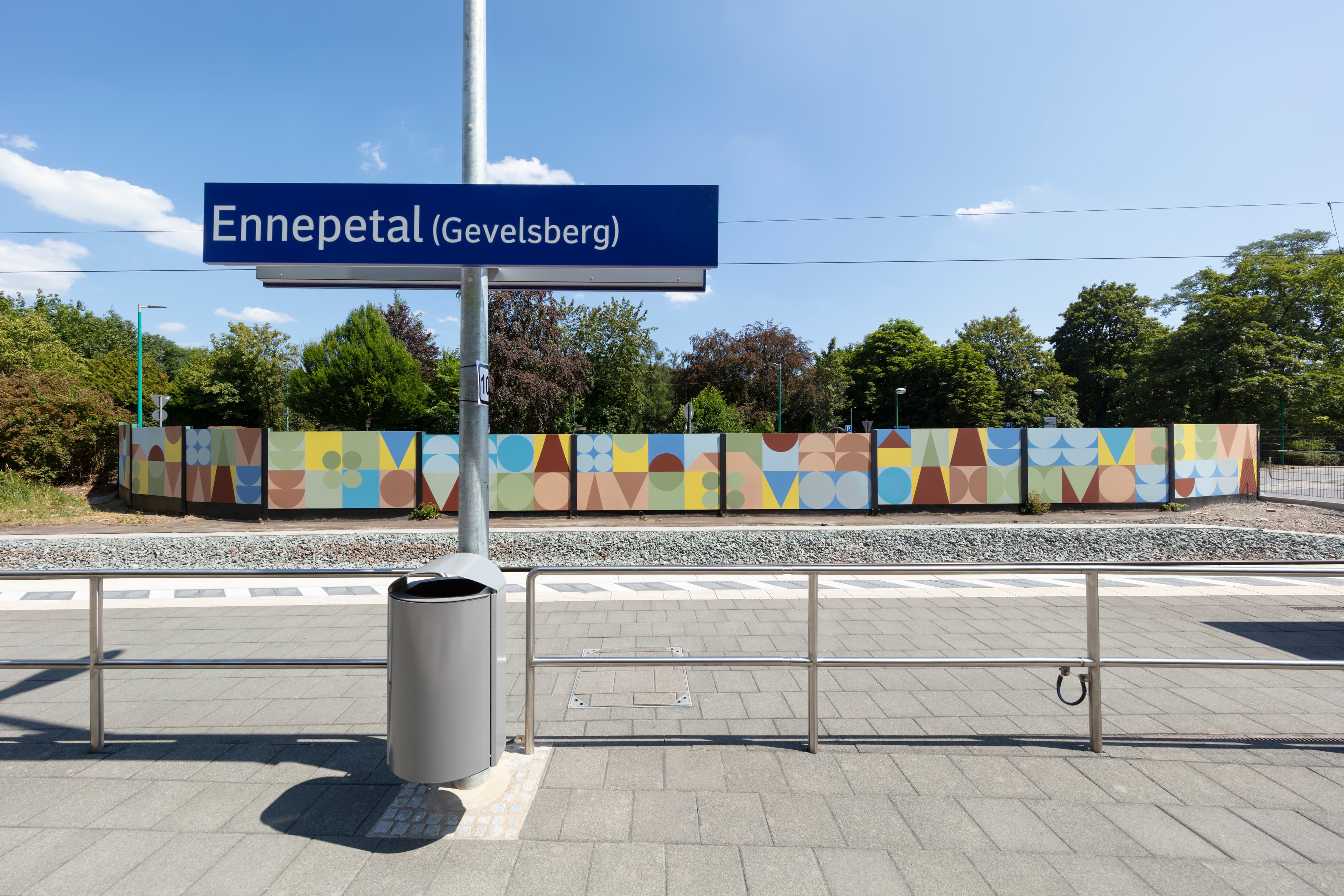 Bahnhofsnamensschild mit der neu gestalteten Sichtschutzwand im Hintergrund.