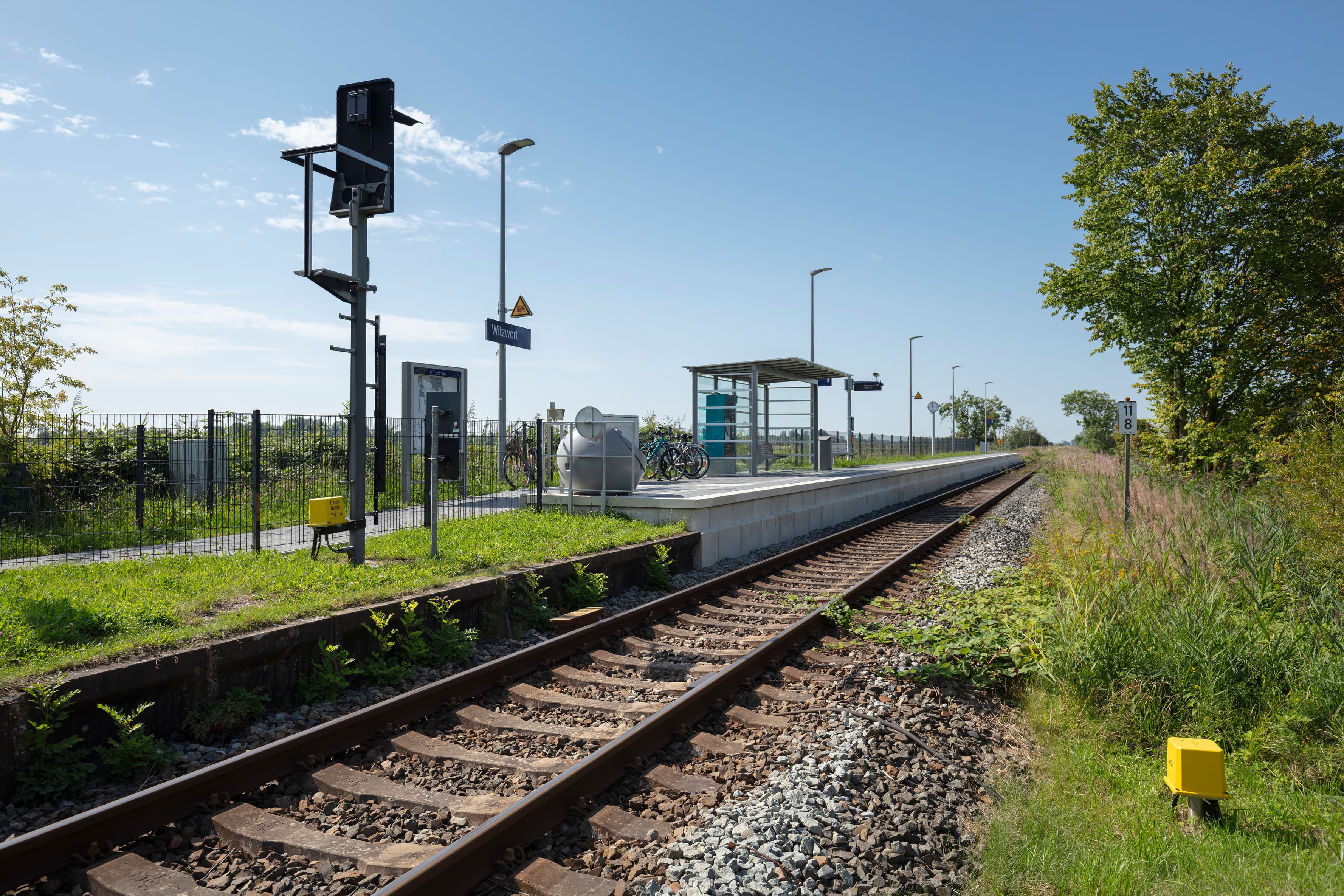 Blick auf den Bahnsteig mit Zugzielanzeiger und neuer Sitzbank. 