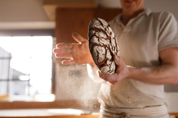 Bäcker klopft Mehl von einem fertigen Laib Brot.