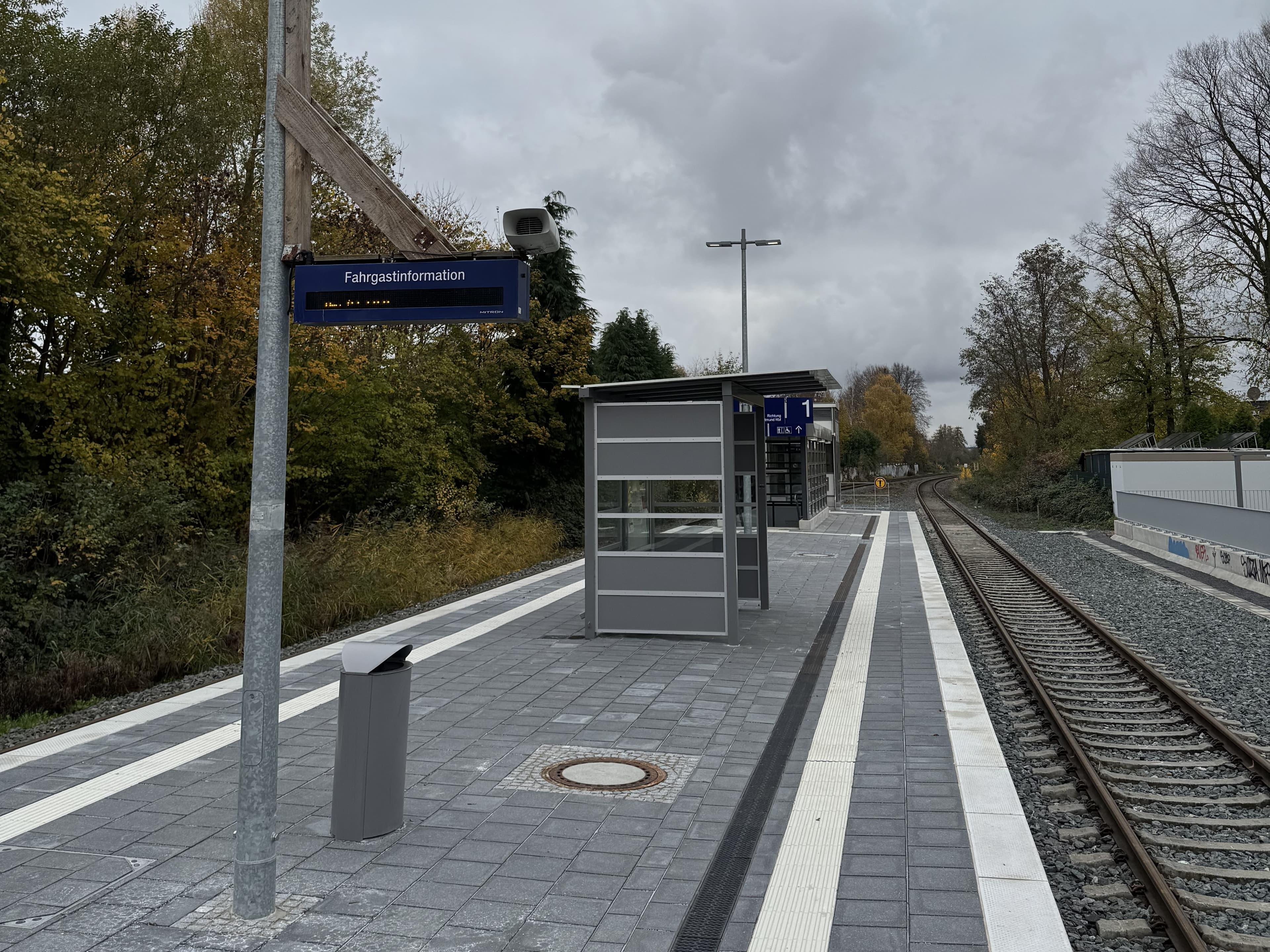 Blick auf den Bahnsteig mit altem Wetterschutz und der alten Fahrgastinformationsanlage (DSA) im Vordergrund.