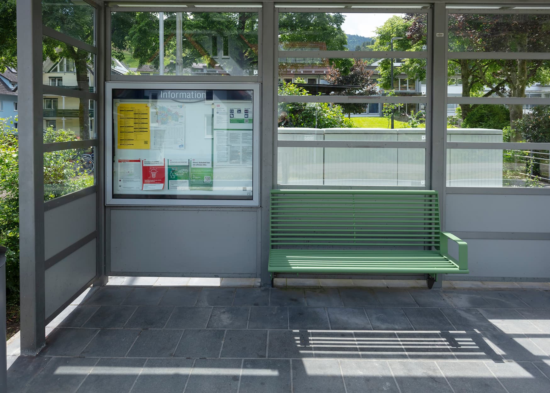 Grüne Sitzbank in einem Wetterschutzhäuschen.