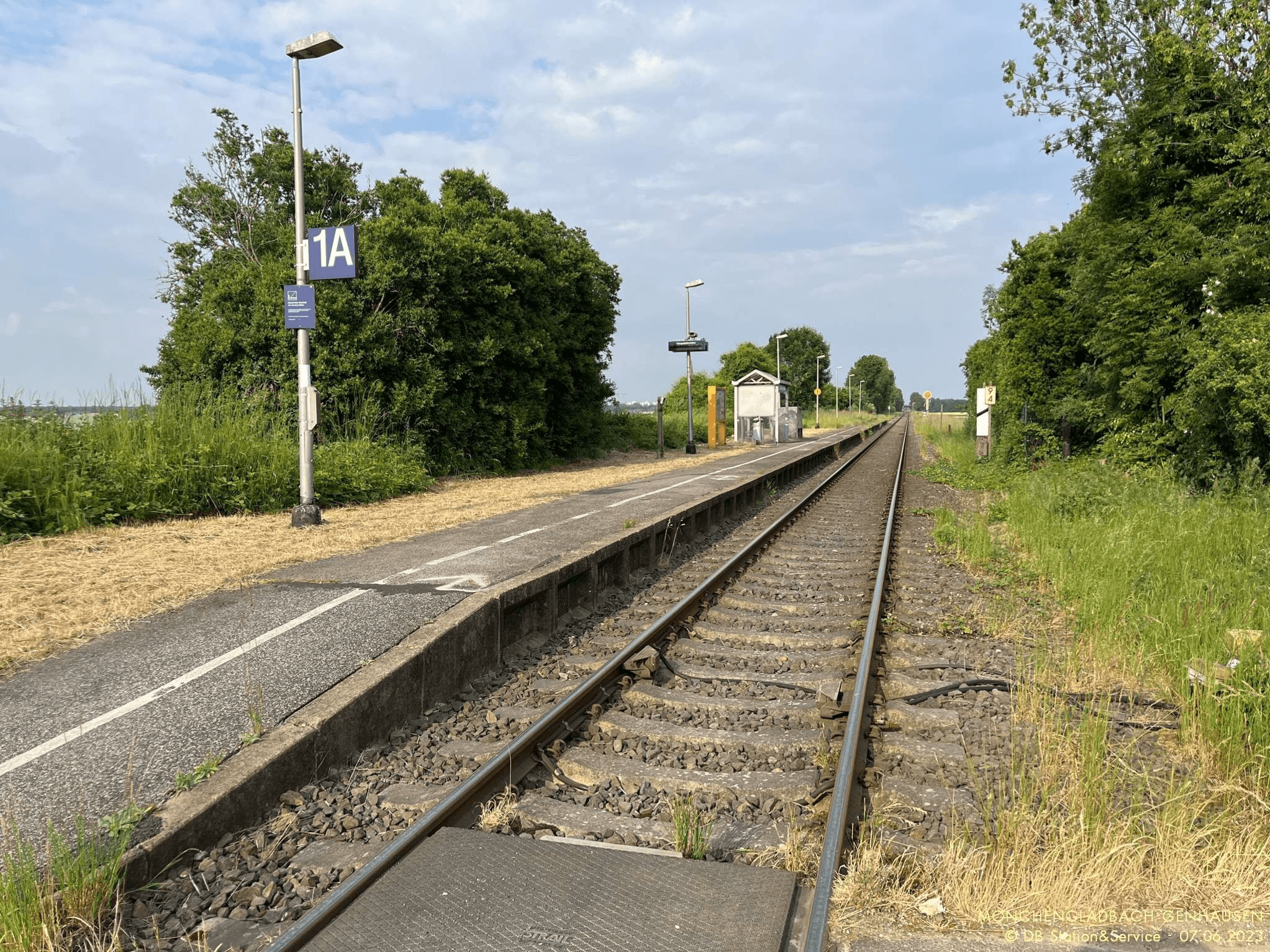 Einfacher Bahnsteig neben Gleisen ohne Blindenleitstreifen und ohne Geländer.