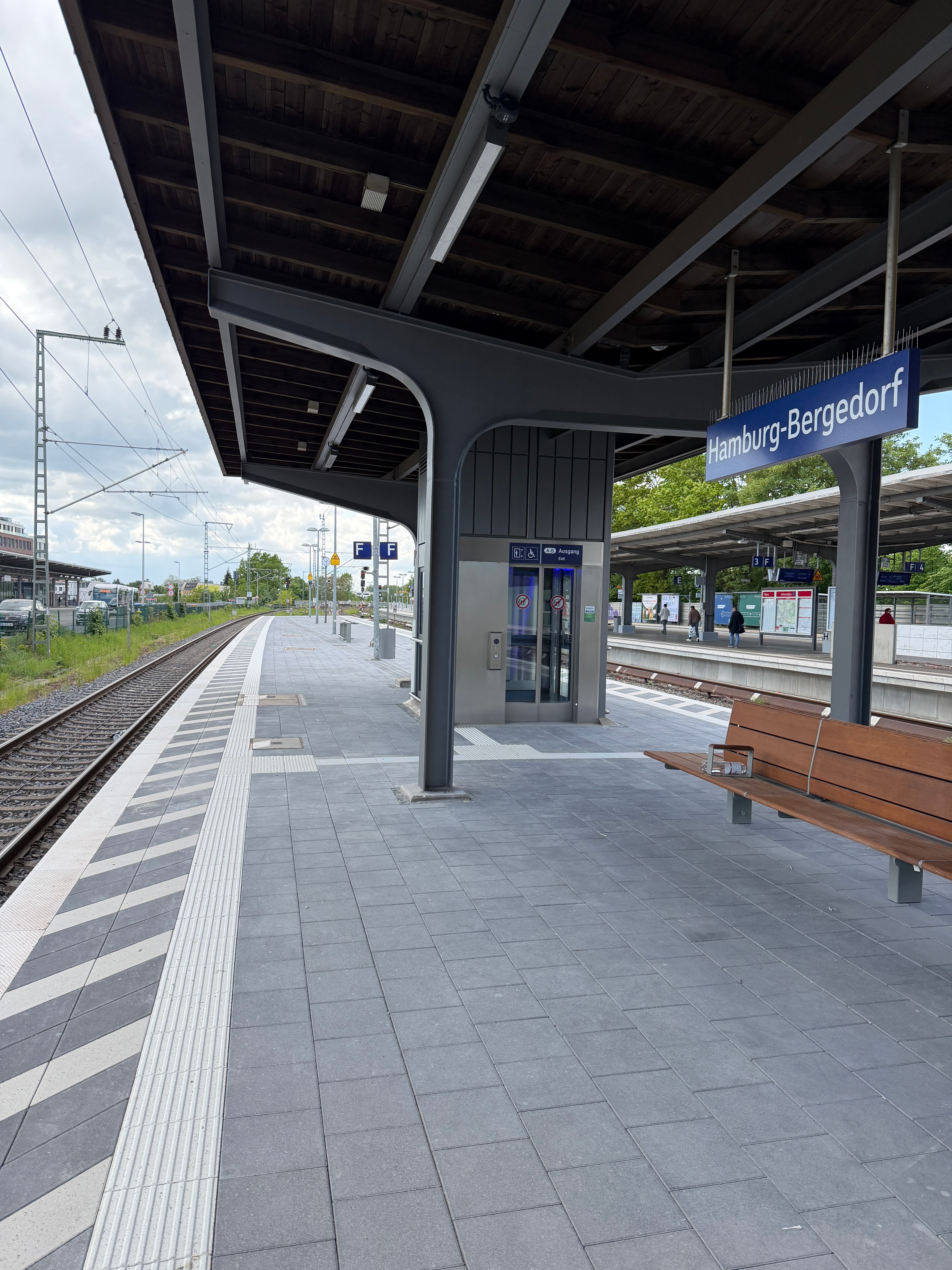 Auf dem neuen Bahnsteig steh eine hölzerne Sitzbank im Hintergrund der Aufzug.