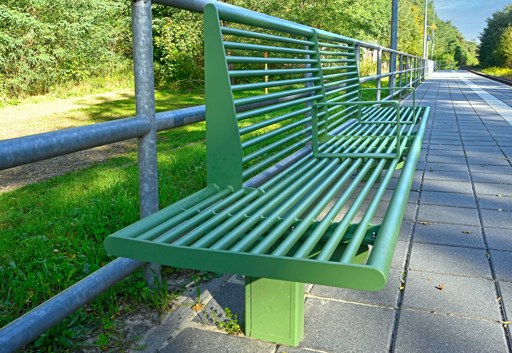 Grüne Sitzbank am Bahnsteig.