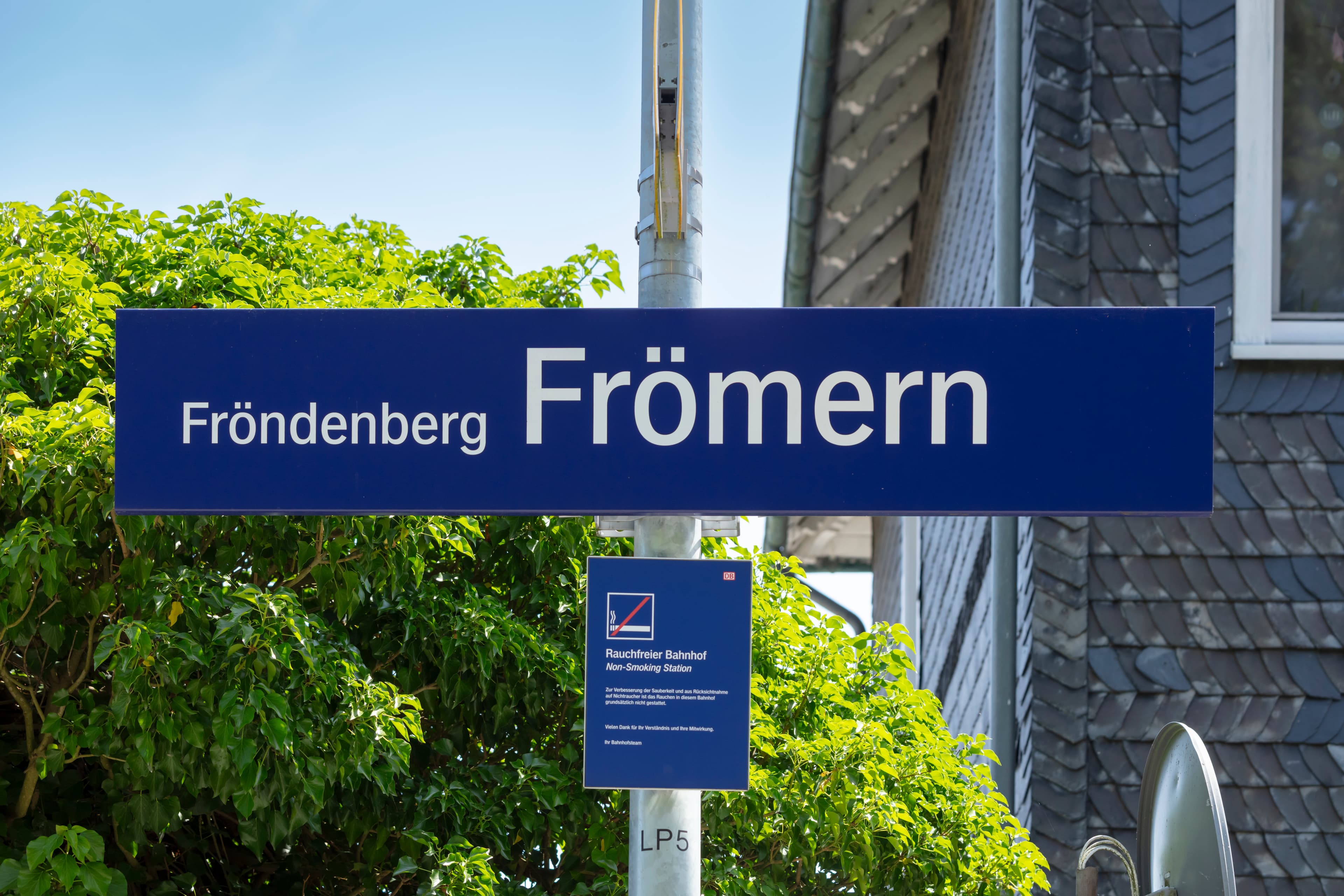 Blick auf das Bahnhofsschild und dem neuen Hinweisschild für Rauchverbot.