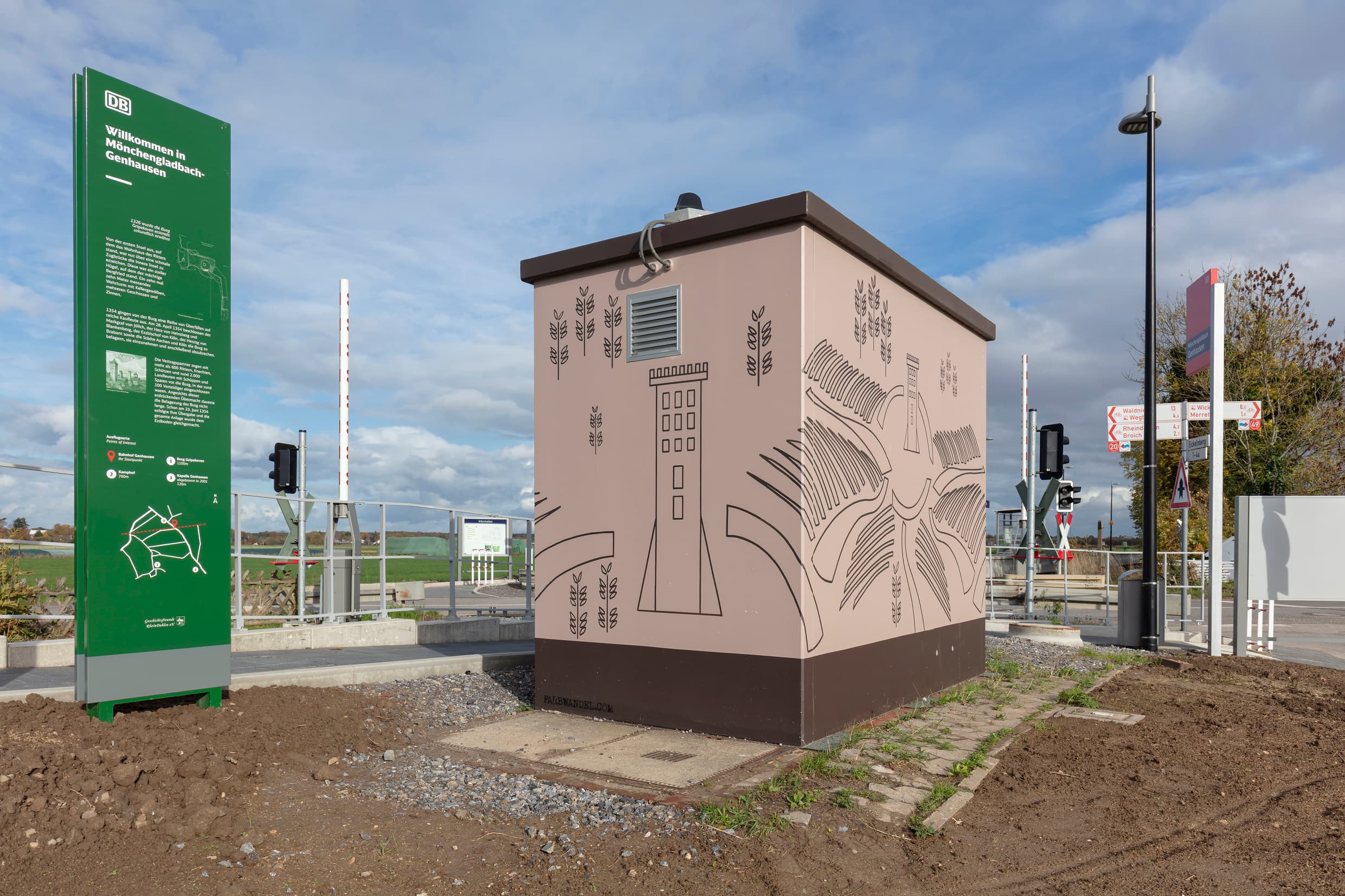 Neu gestaltetes Schalthaus. Links davon ist eine grüne Informationstafel. Im Hintergrund ist ein Bahnübergang zu erkennen.