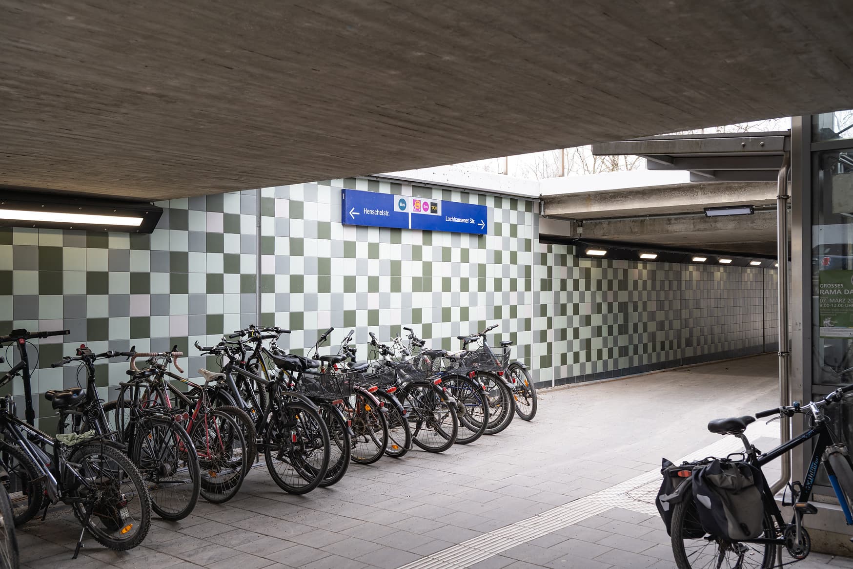 Blick auf eine Personenunterführung. Blaue Beschilderung an grün/weiß gefliesten Wänden. Viele Fahrräder sind an einer Fahrradabstellanlage geparkt.