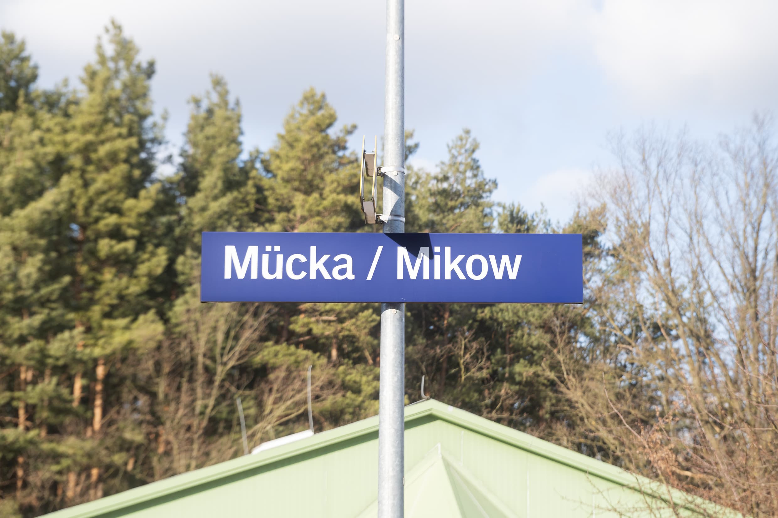 Blaues Bahnhofsnamensschild Mücka ist zweisprachig ausgeführt - auf sorbisch Mikow