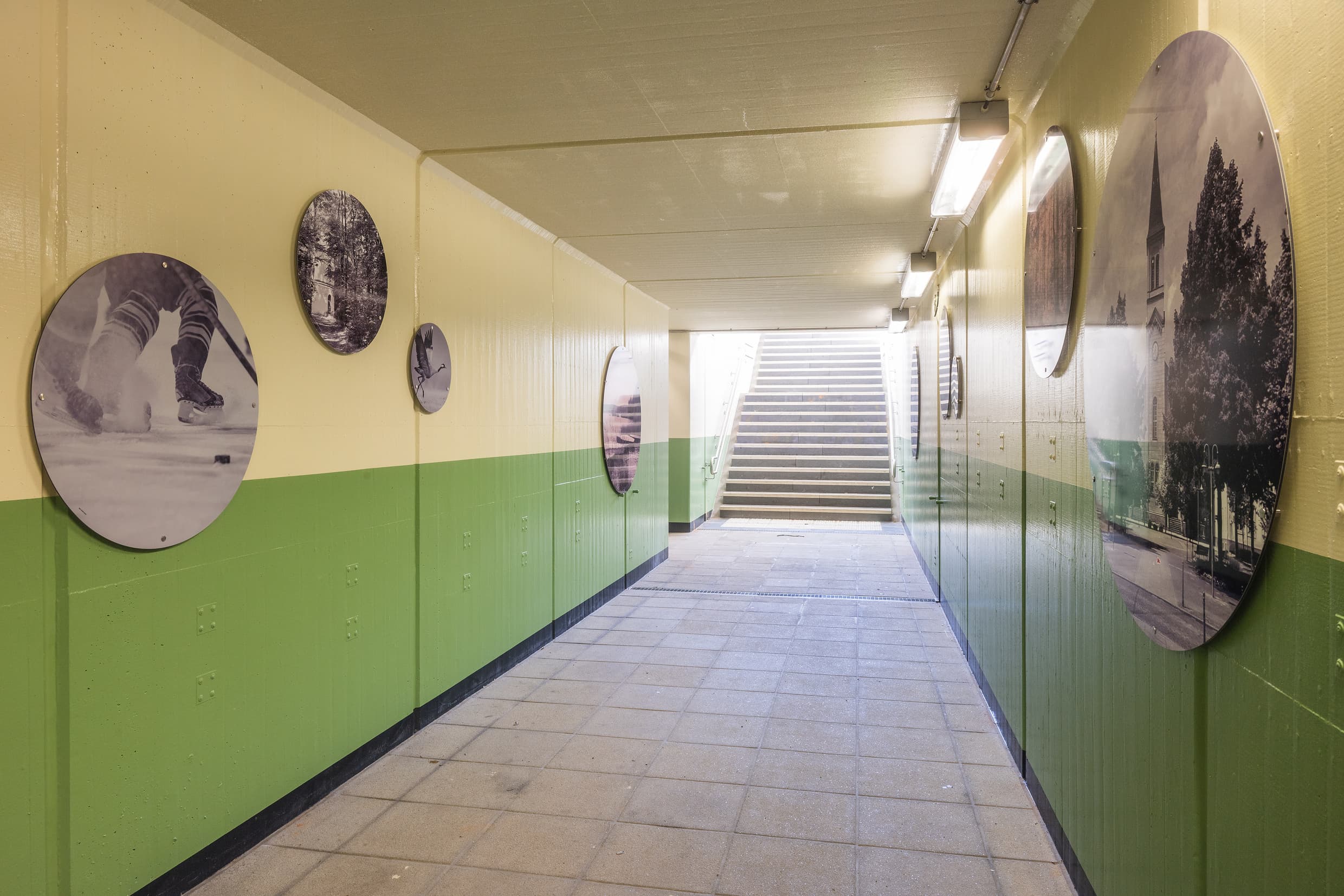 Blick in die gestaltete Personenunterführung: Die Wände sind zweifarbig in seichten Gelb und Grünton gestrichen. Darauf aufgebracht sind ovale Boards mit regionalen Motiven.