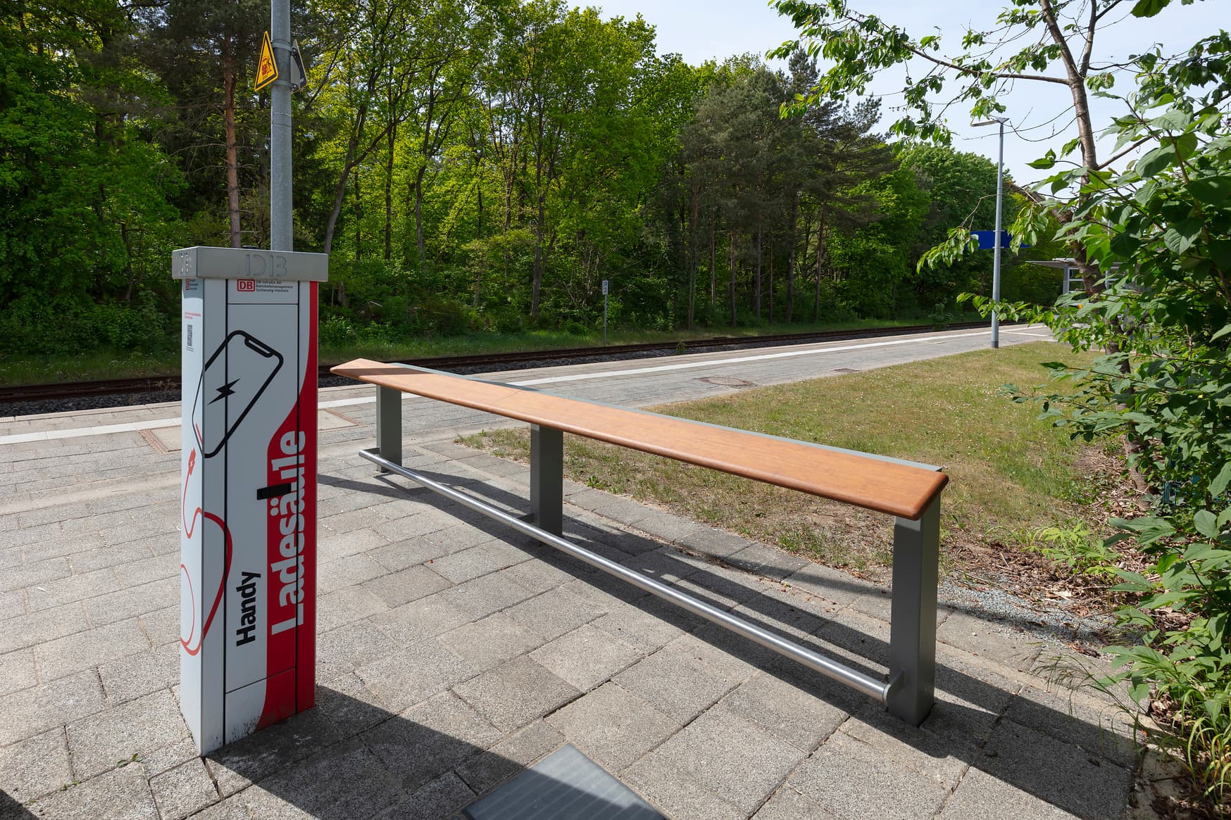 Eine solarbetriebene Handyladesäule am Bahnsteig neben einem Anlehner.