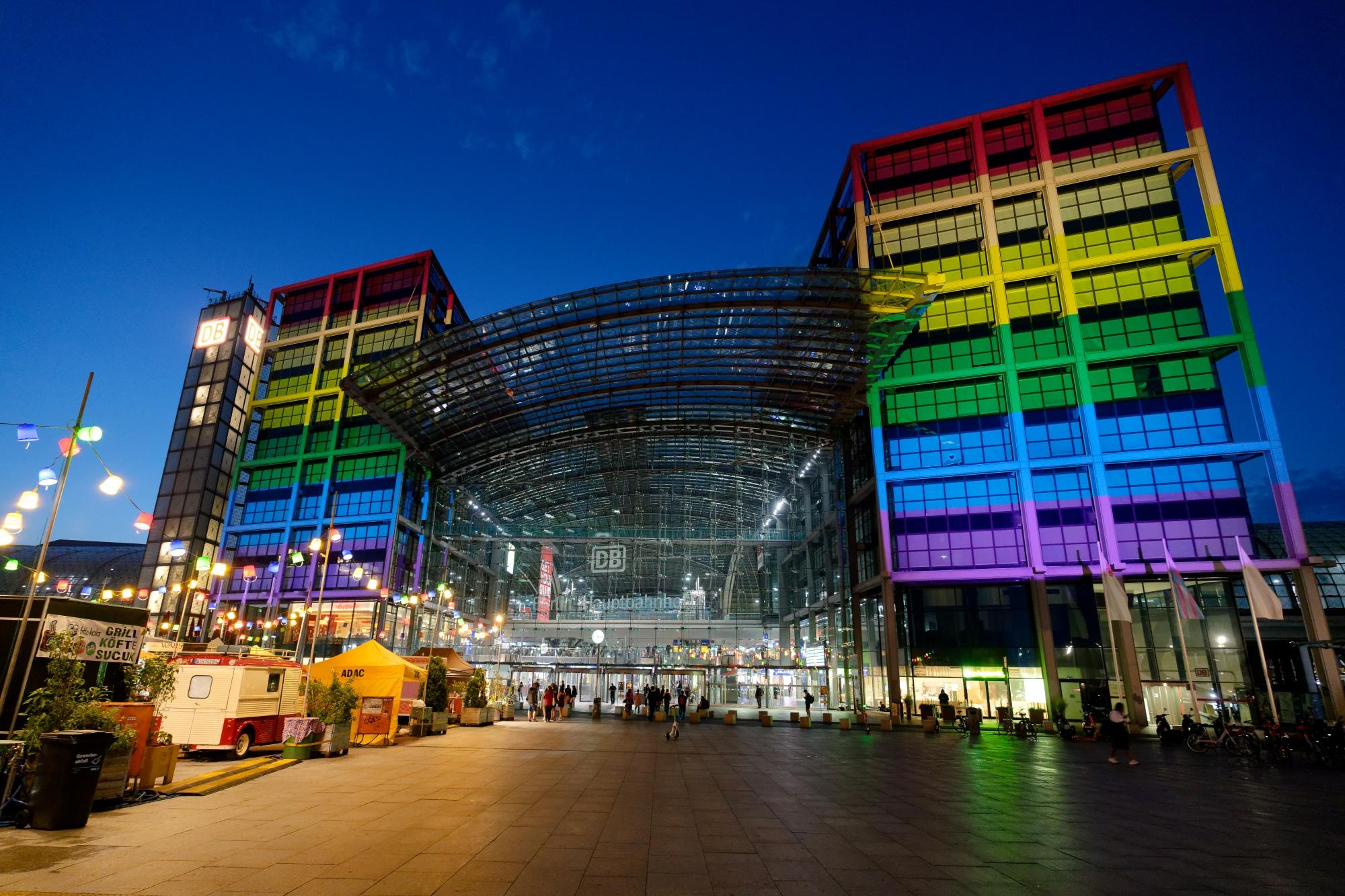 Der Berliner Hauptbahnhof erstrahlt vor dem Nachthimmel in den Regenbogenfarben der queeren Community.	