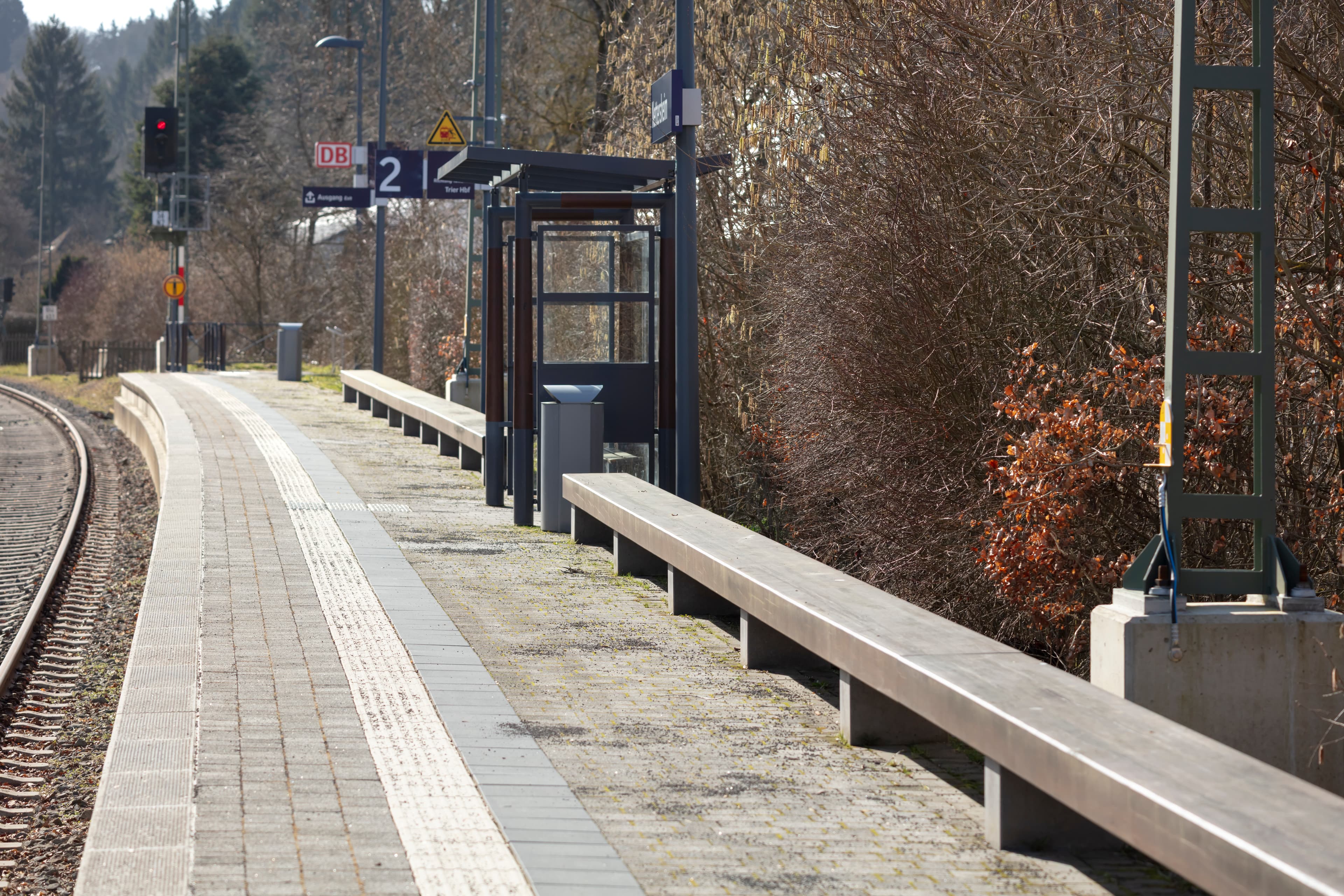 Sitzbänke an einem Bahnsteig. Dazwischen ein Wetterschutzhäuschen. Links vom Bahnsteig befindet sich das Gleis.