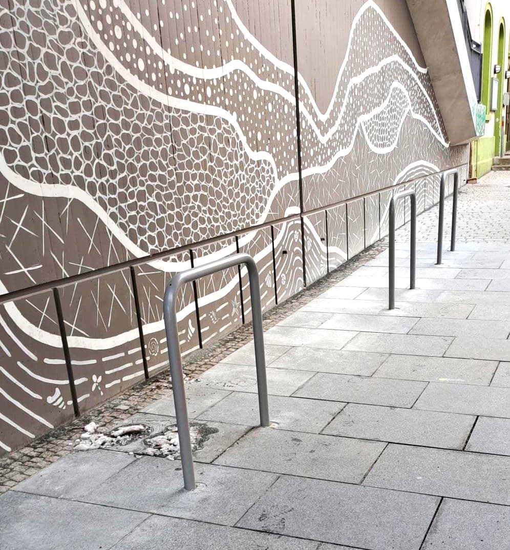 Drei Fahrradbügel parallel zur gestalteten Wand im Zugangsbereich der Verkehrsstation