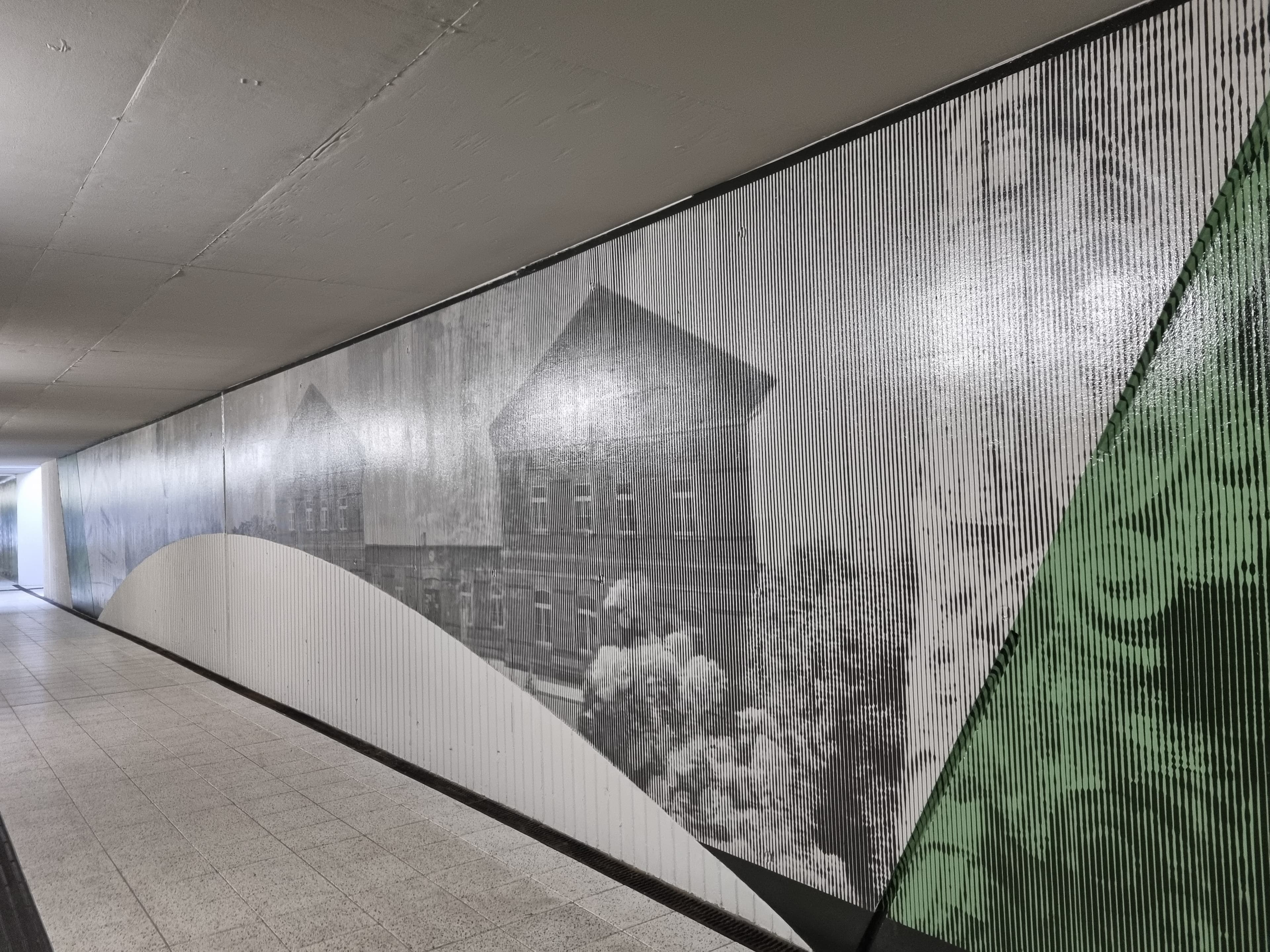 Zu sehen ist ein Ausschnitt einer Tunnelwand mit einem Häuser-Bilder der Stadt Borsdorf. Baulichen Besonderheiten des Tunnels, wie ein Bogen an der Wand, sind in die Gestaltung integriert.
