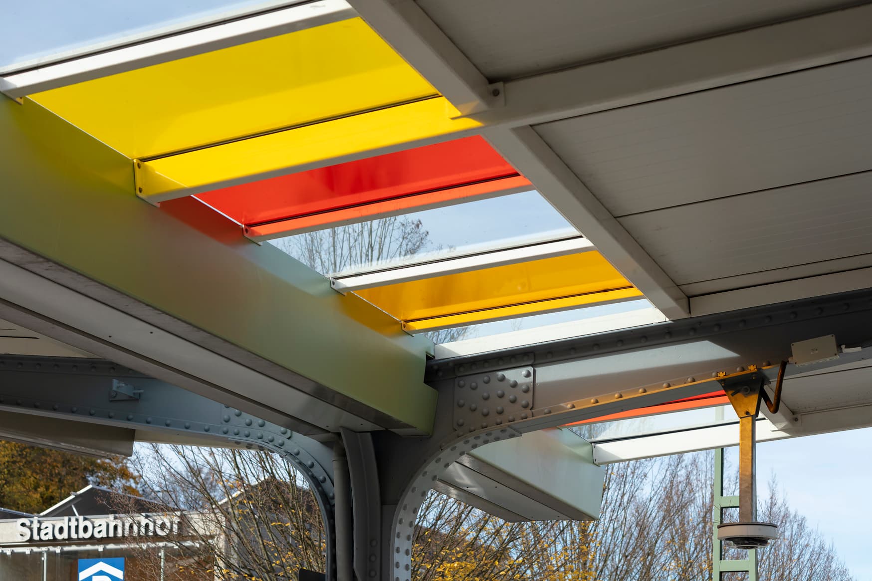 Die rot, gelb, organgne farblichen Folierung der Glaselemente im Bahnsteigdach.