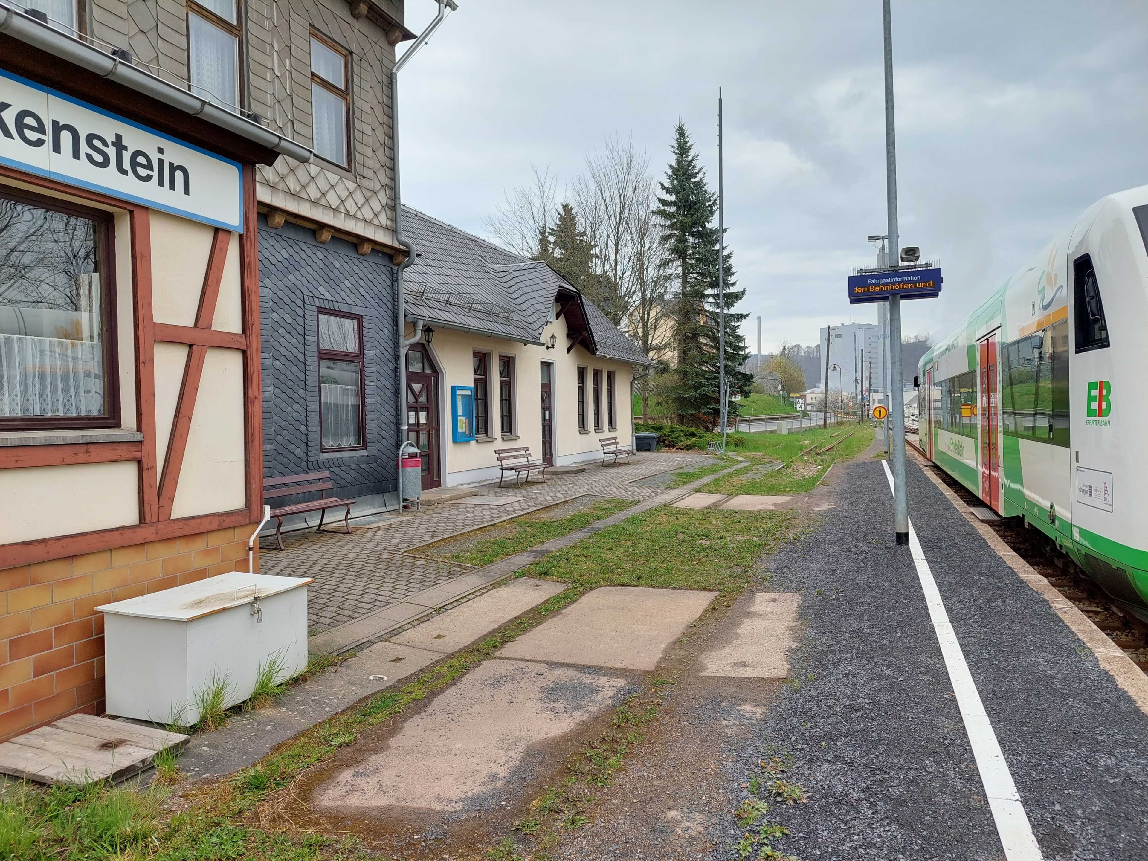 Der unbefestigte Bahnsteig mit der alten Ausstattung vor dem Umbau 2023 - inkl. Blick auf das ehemalige Empfangsgebäude und einen haltende Zug der Erfurter Bahn.