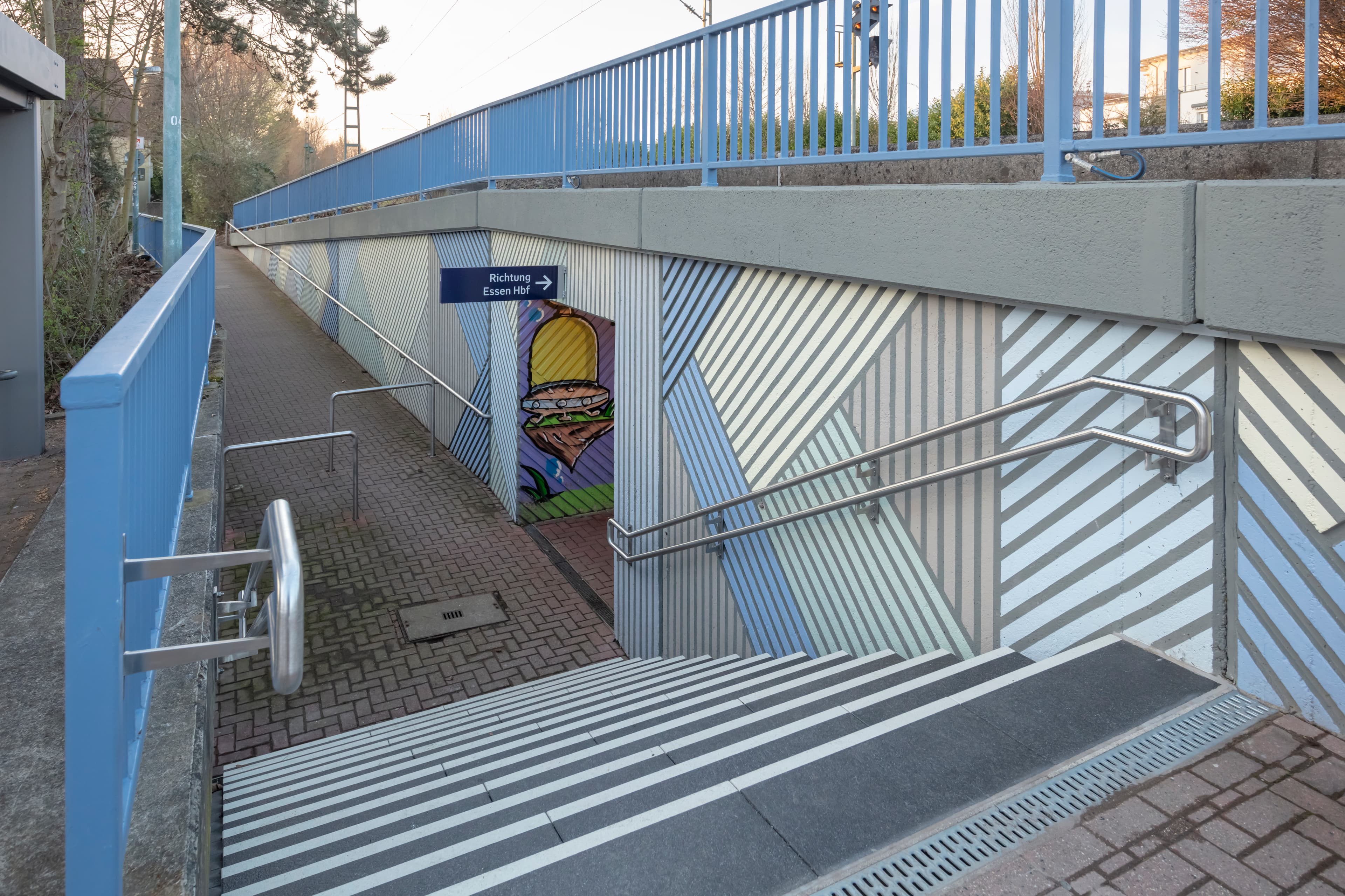 Blick auf eine runterführende Treppe. Rechts und links Wände mit Handläufen.