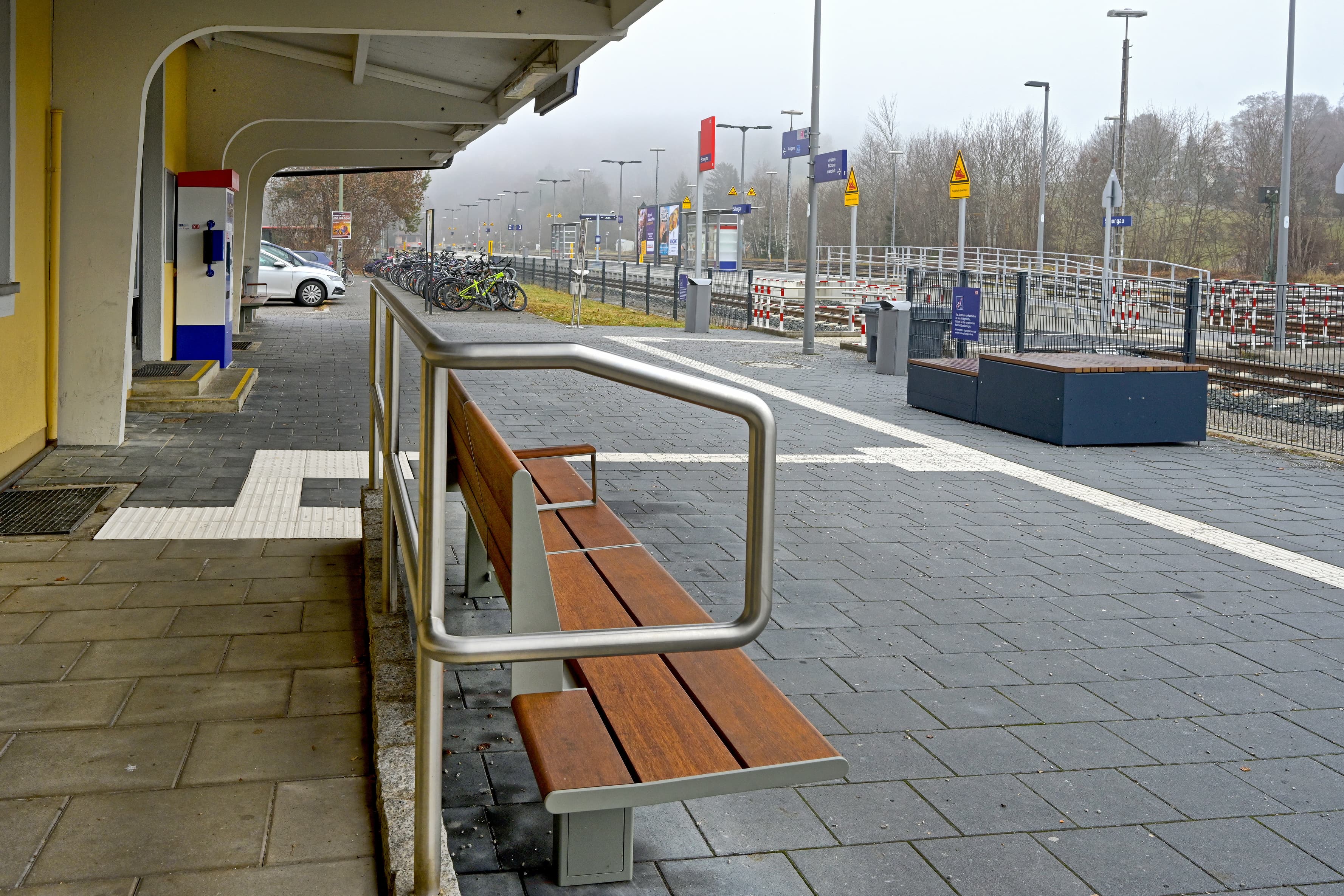 Abgebildet eine Bank. Links das Dach eines Gebäudes. Rechts ein Podest, das als Sitzgelegenheit dient.