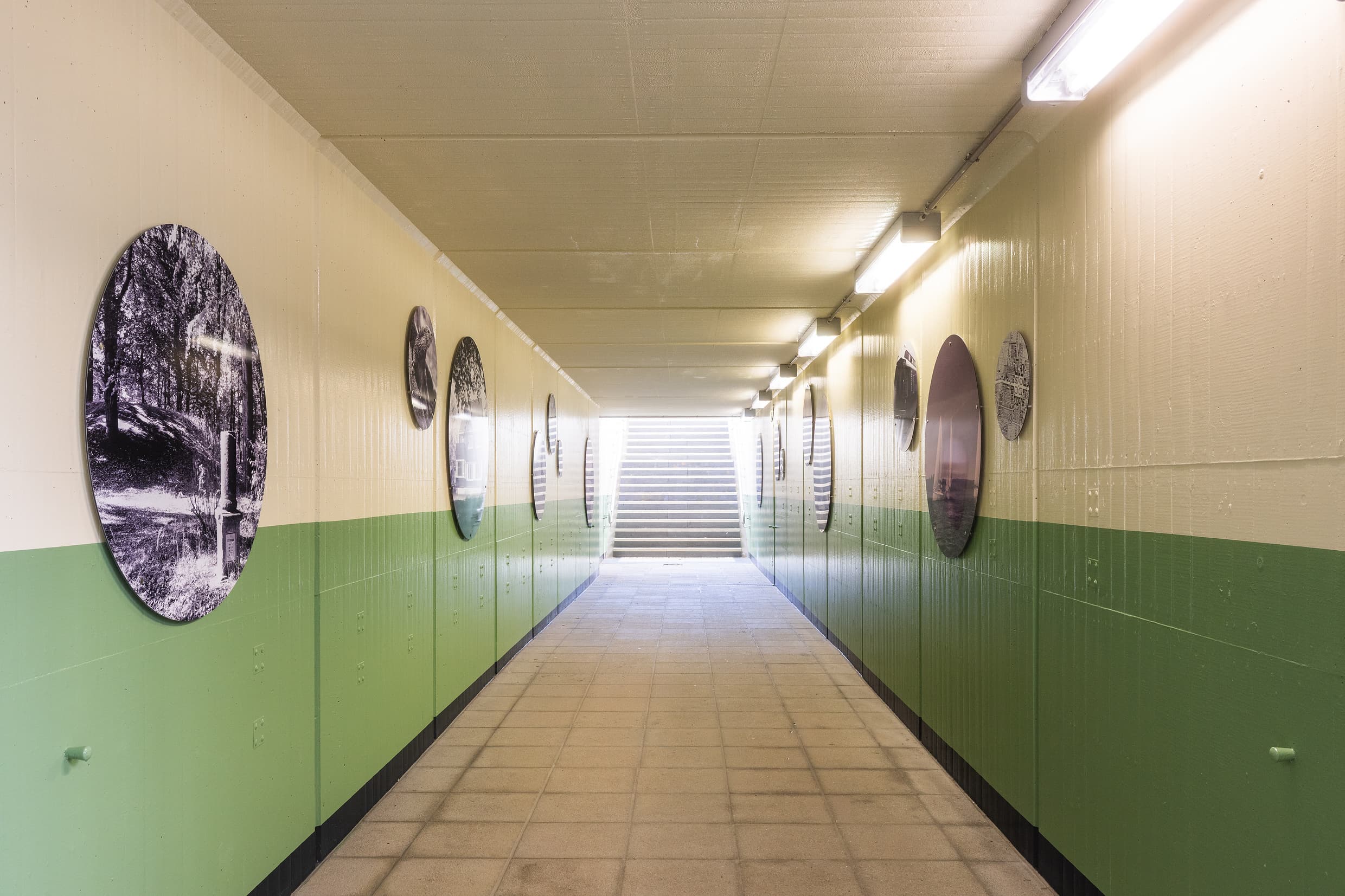 Blick in die Personenunterführung: Untere Hälfte grün, obere Hälfte hellbeige gestrichen. Zusätzlichen sind runde Boards mit regionalen Motiven in schwarz/Weiß angebracht worden