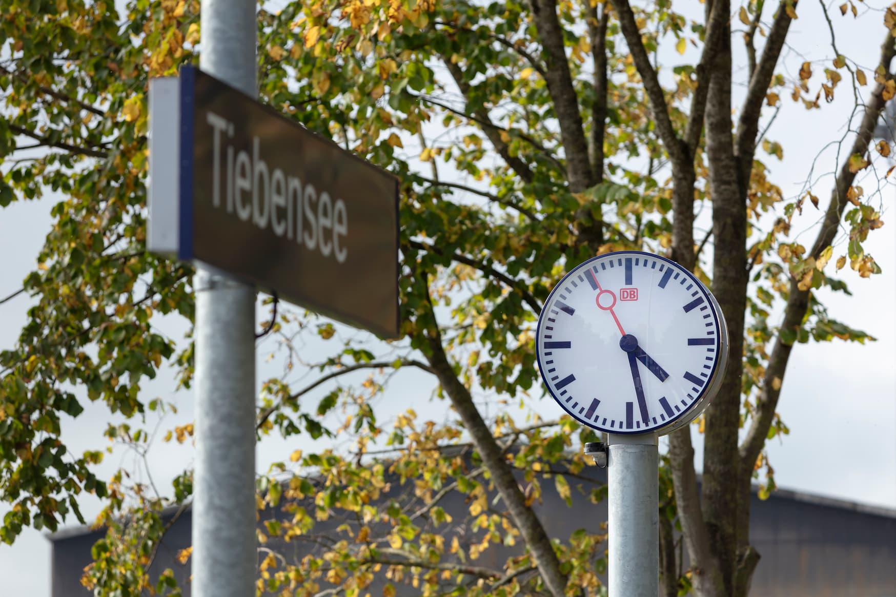 Bahnhofsuhr auf einer Stele daneben das Bahnhofsschild Tiebensee auf einer eigenen Stele.