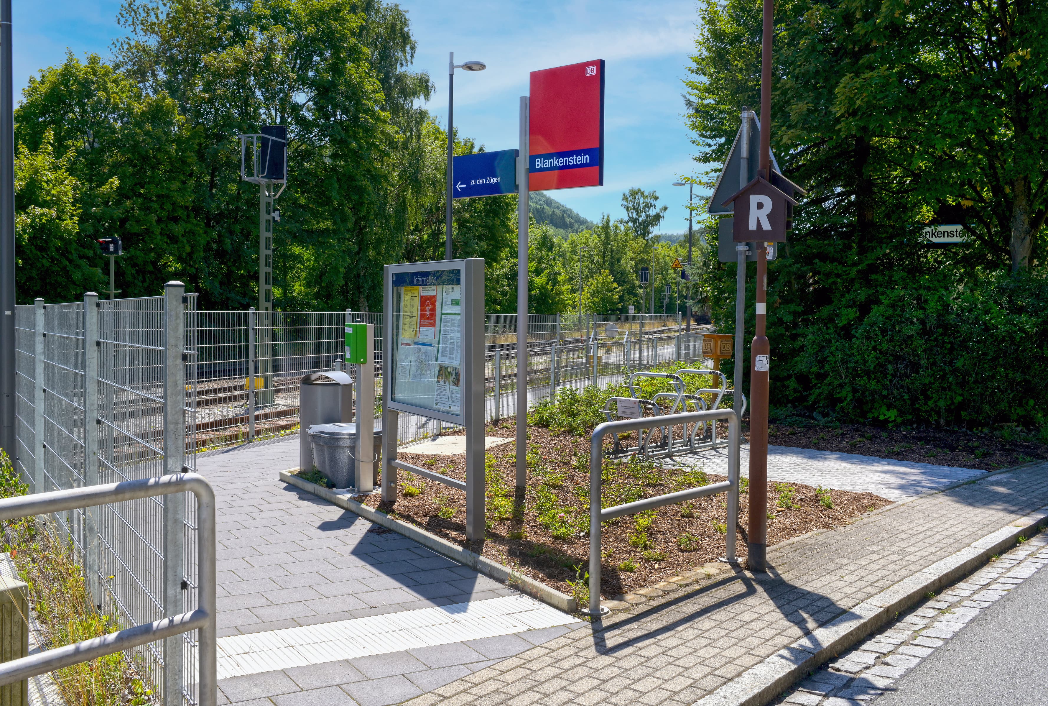 Der Zugang auf den neu gebauten Bahnsteig ist barrierefrei. Auf der rechten Seite steht die Bahnhofsfahne und die Vitrine. Auf der linken Seite befindet sich ein Zaun als Abgrenzung zu den Gleisen.