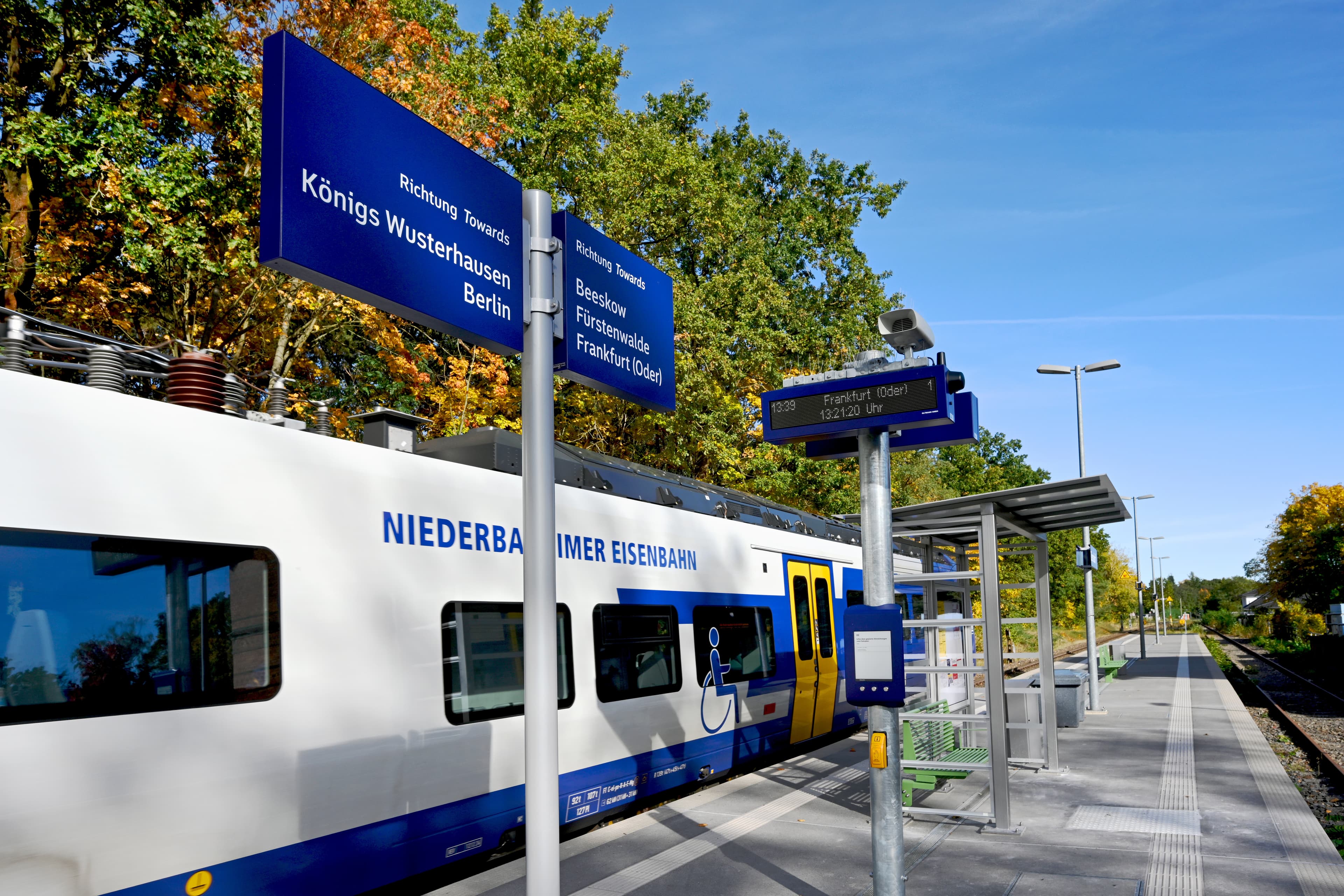 Blick auf einen Bahnsteig mit Beschilderungen, links hält ein Zug.