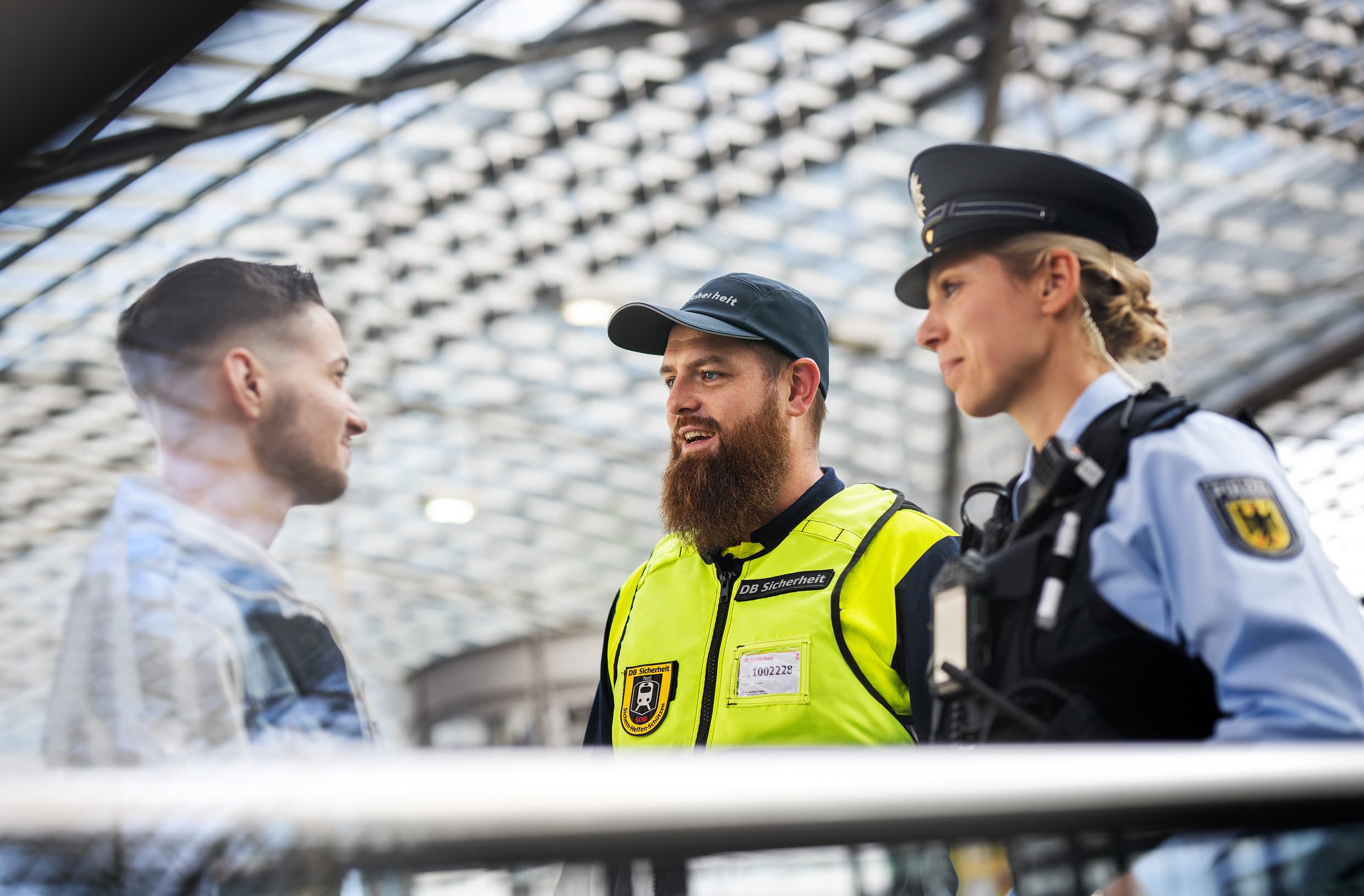 Eine Frau von der Bundespolizei und ein Mann der DB Sicherheit sprechen gemeinsam mit einem Reisenden an einem Bahnsteig.