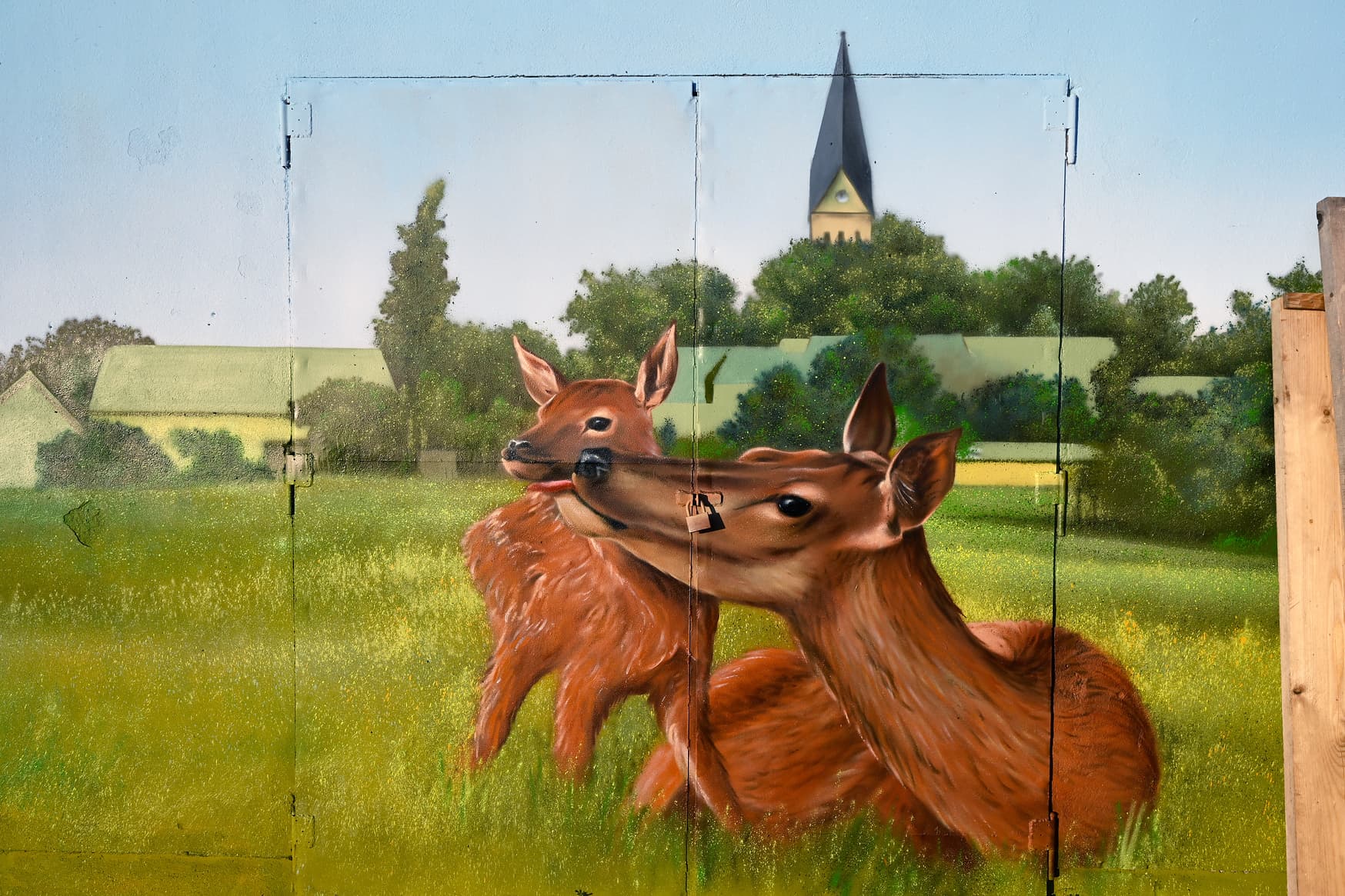 Das bemalte Nebengebäude zeigt ein Reh mit Kitz auf einer Wiese mit dem historischen Ortskern im Hntergrund.