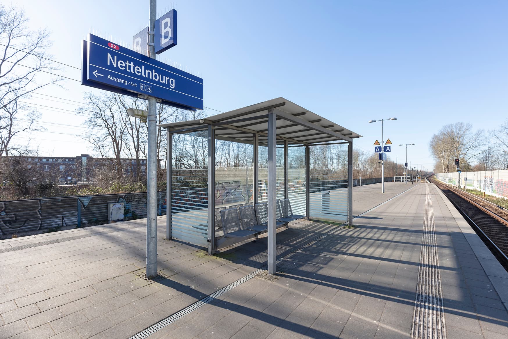 Wetterschutzhaus zu beiden Seiten des Bahnsteiges. Daneben das blaue Bahnhofsschild und Gleisabschnittsanzeigen.