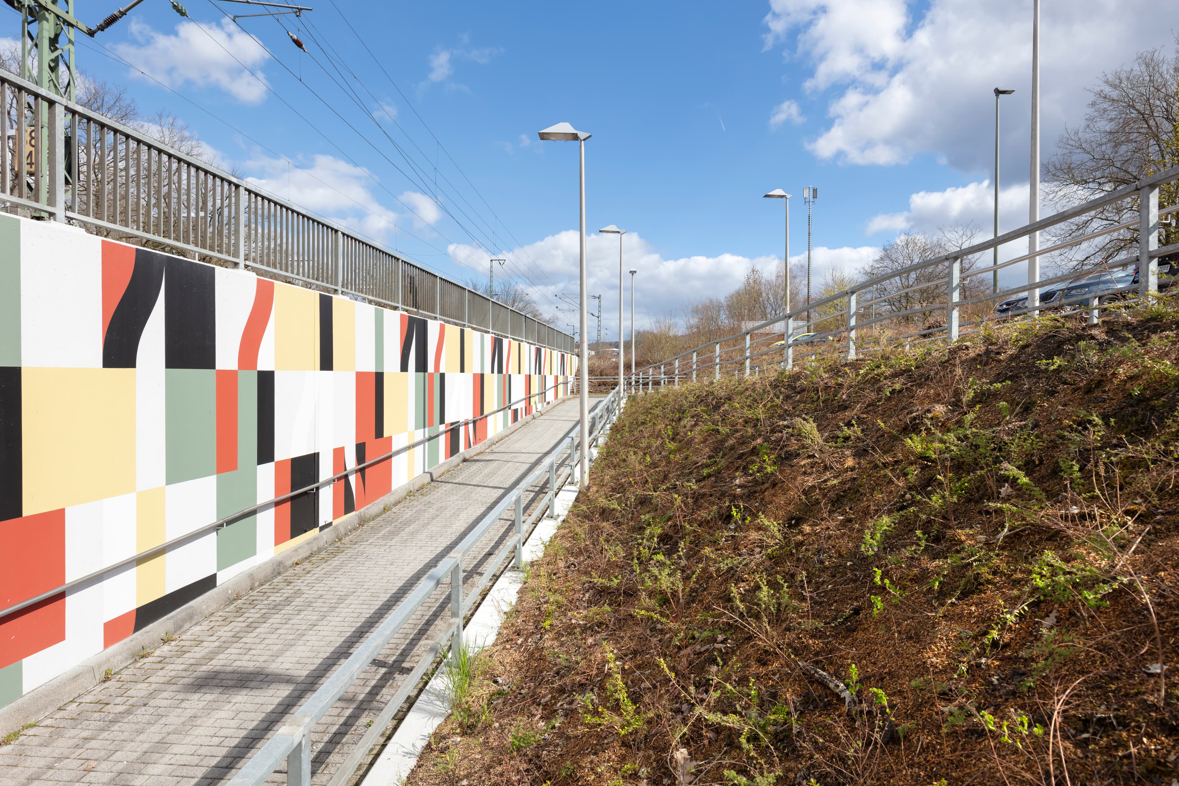 Grünflächen an dem Zugang zur Personenunterführung. Links eine bunt gefliest Wand.