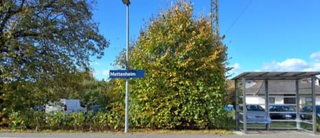 Bahnsteig mit Bahnhofsschild. Dahinter die neue Begrünung in Form von gepflanzten Büschen.