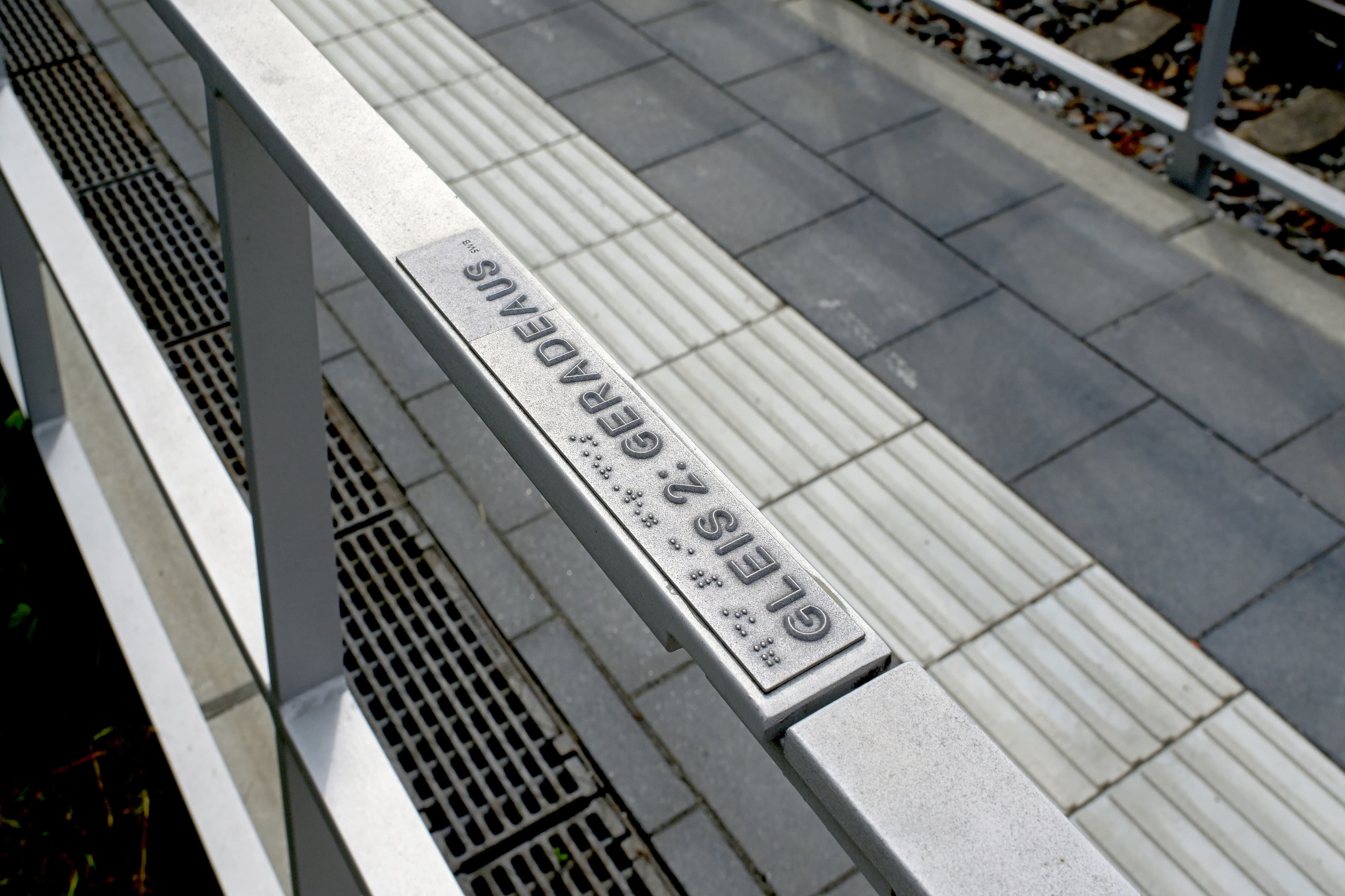Braille-Schrift auf einem Geländer eines Bahnsteigs.