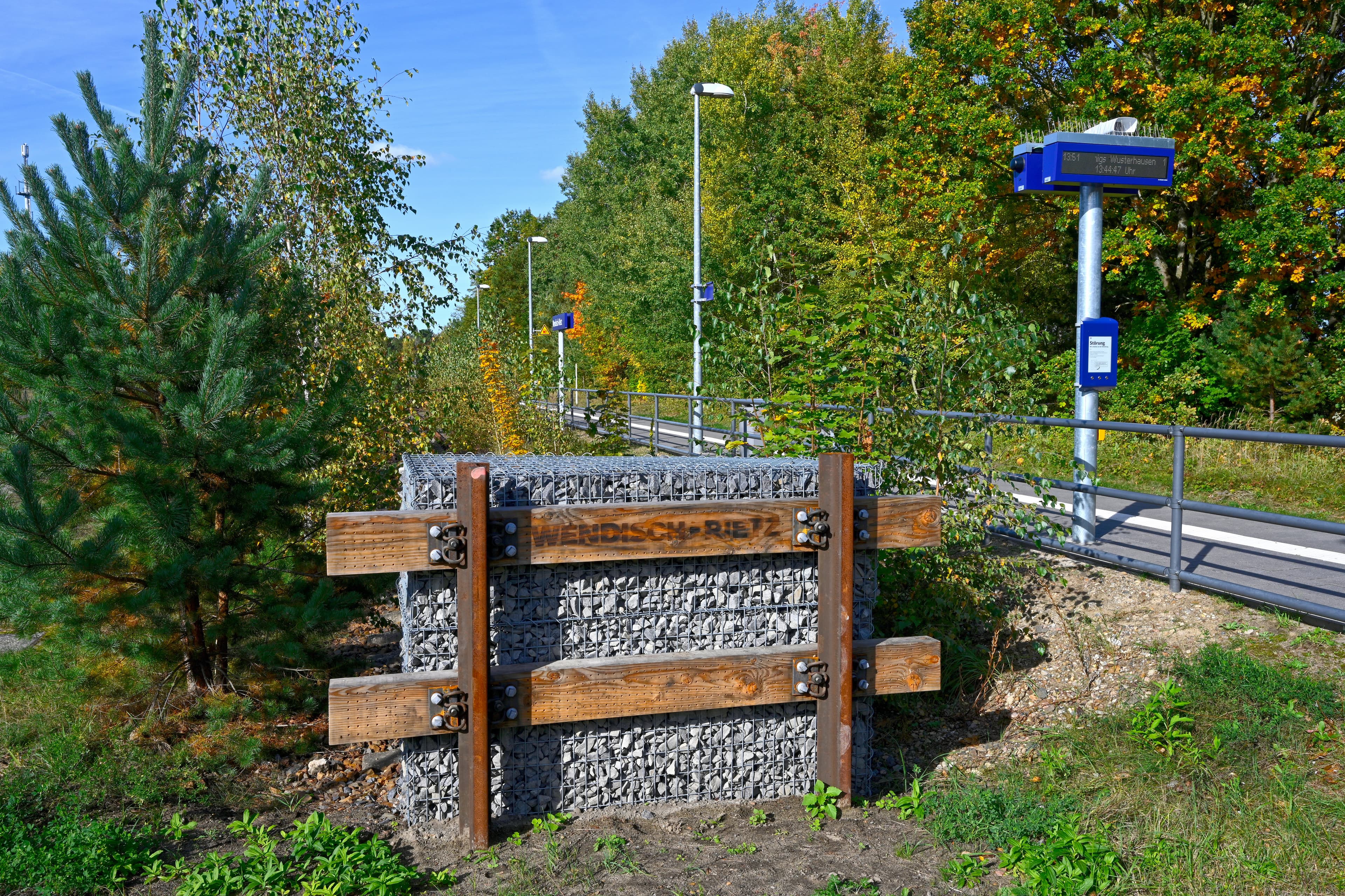 Ein Bahnhofsschild aus Holz und Stein vor dem Bahnsteig.