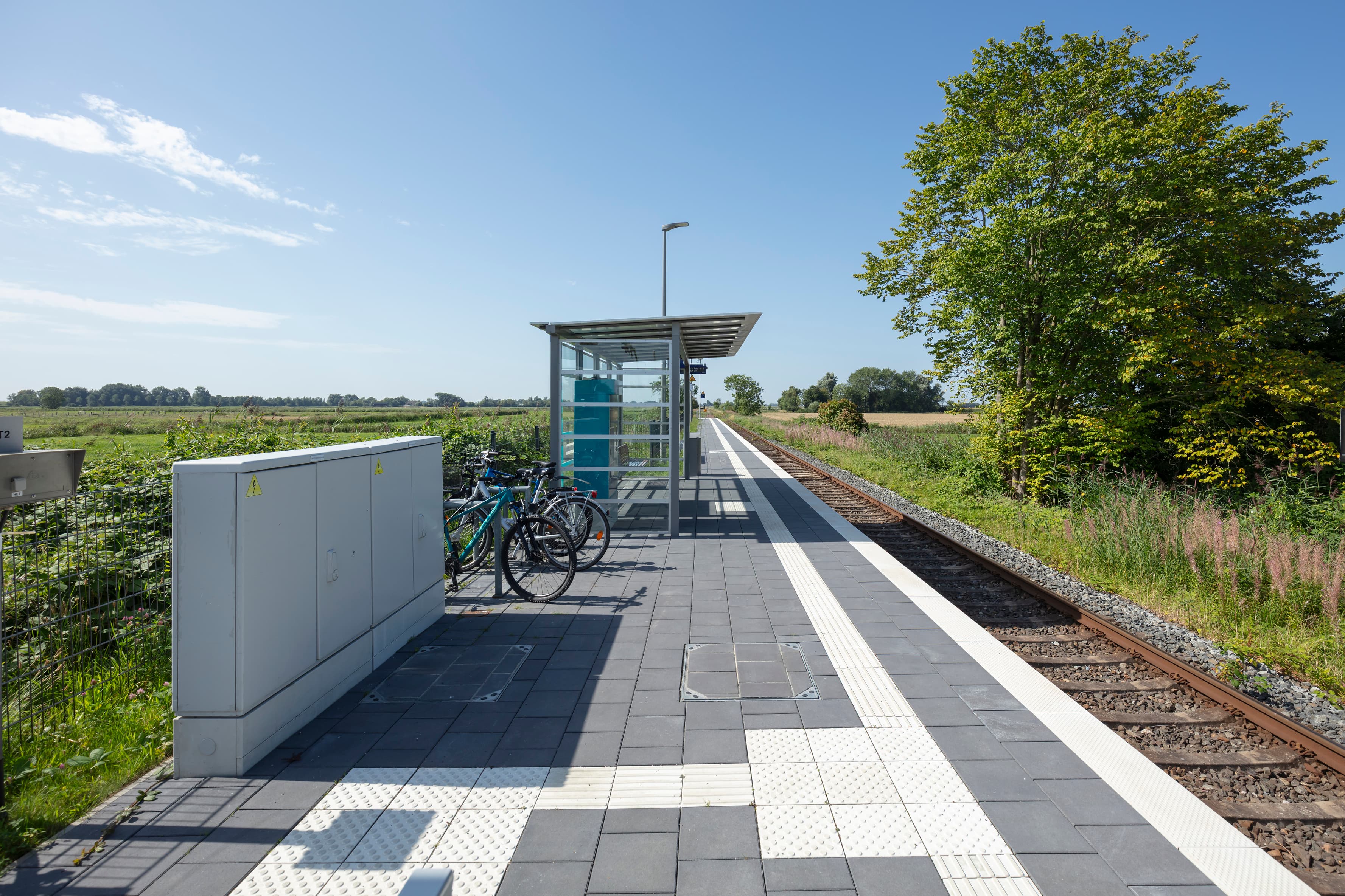 Blick auf den neu gestalteten Bahnsteig mit Zugzielanzeiger im Vordergrund und Marschlandschaft im Hintergrund.