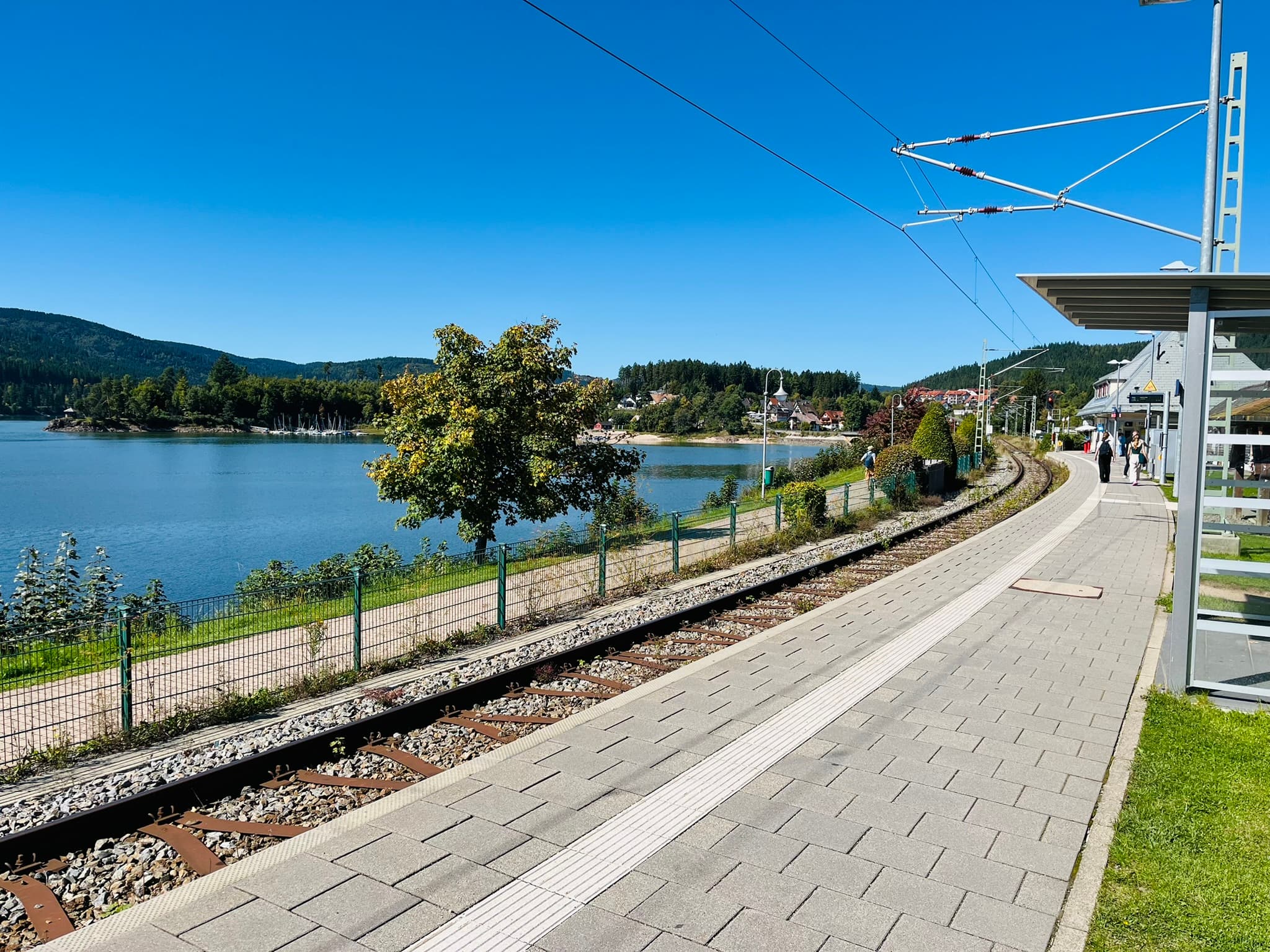 Kurvig verlaufender Bahnsteig des Bahnhofs Schluchsee mit Blick auf die Gleise, den See und die umliegende Schwarzwaldkulisse,
