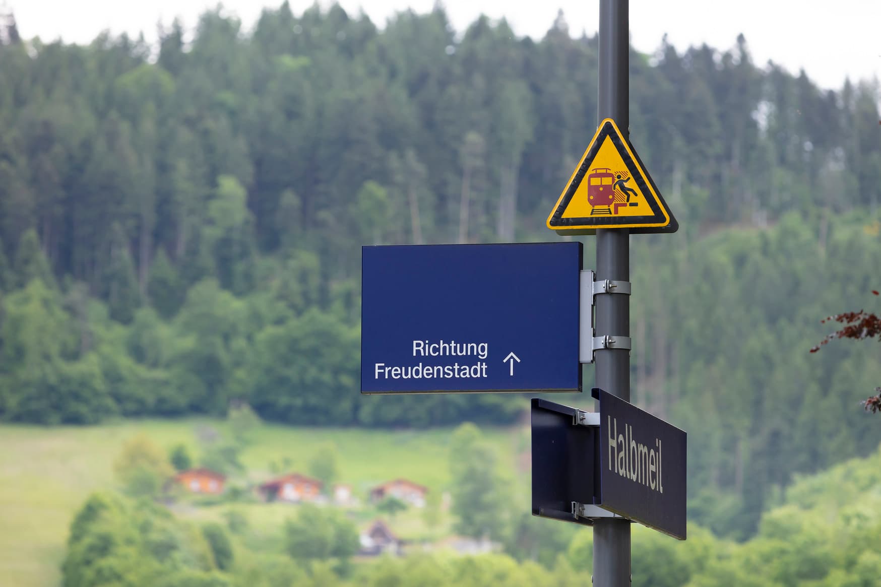 Blaues Schild mit weißer Schrift "Richtung Freudenstadt" und Richtungspfeil oberhalb des Bahnhofsschild.