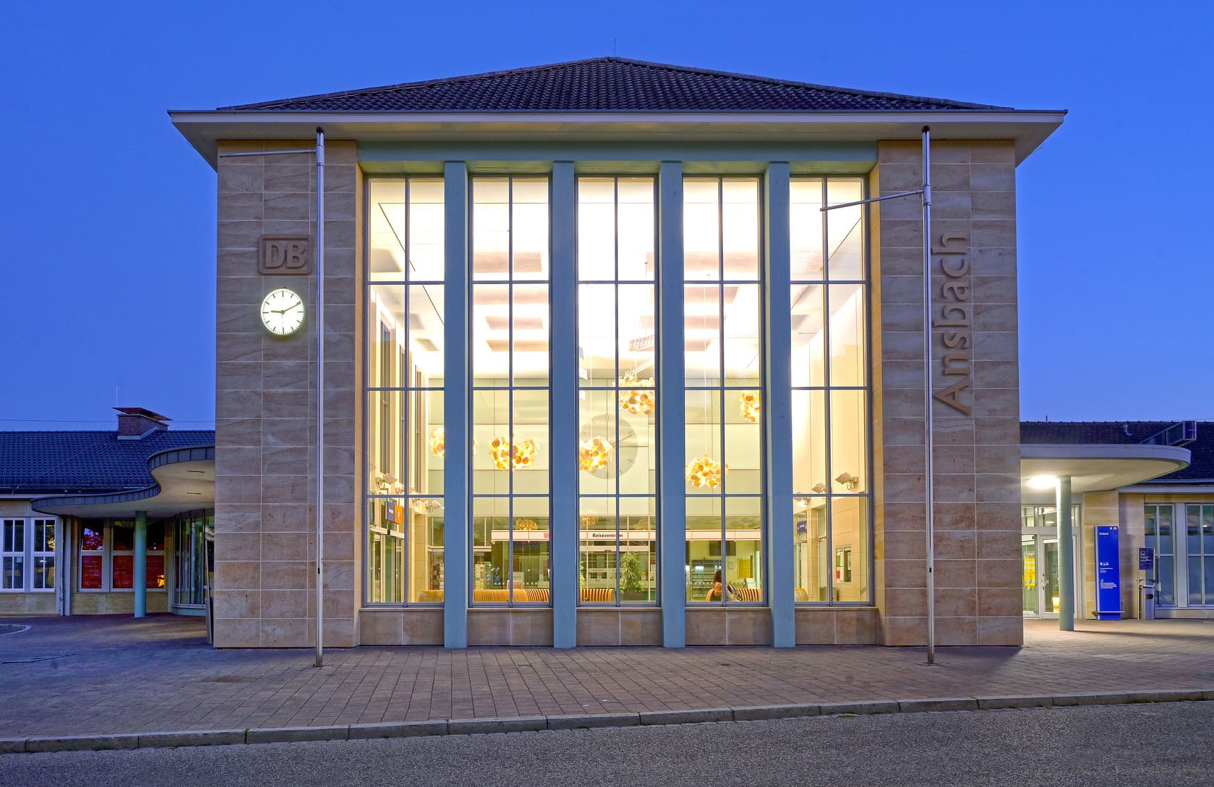 Hell erleuchtetes Empfangsgebäude. Goldener Schriftzug Ansbach an der Seite des Gebäudes.
