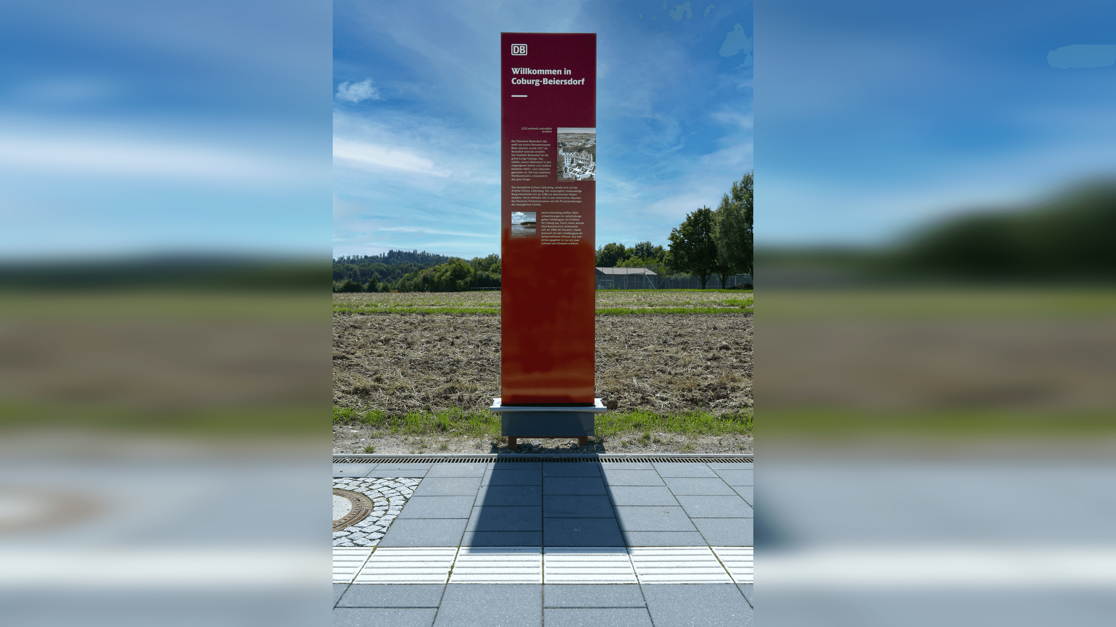 Infoschild vor blauem Himmel. Informationen zu Schloss Callenberg und dem Goldbergsee.