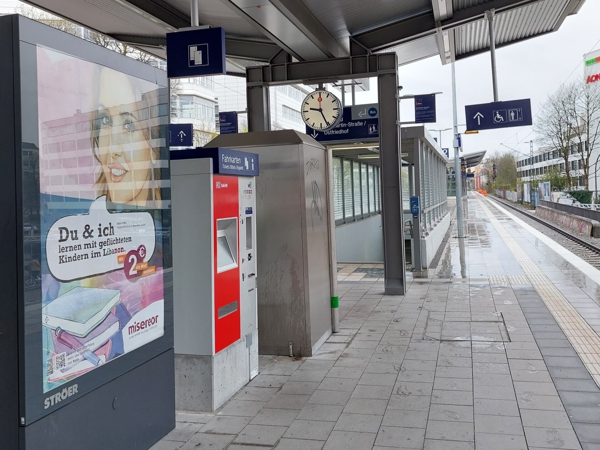 Blick auf den unübersichtlichen Bahnsteig mit Werbetafel, Fahrkartenautomat, Snackautomat und verdeckter Wegeleitung