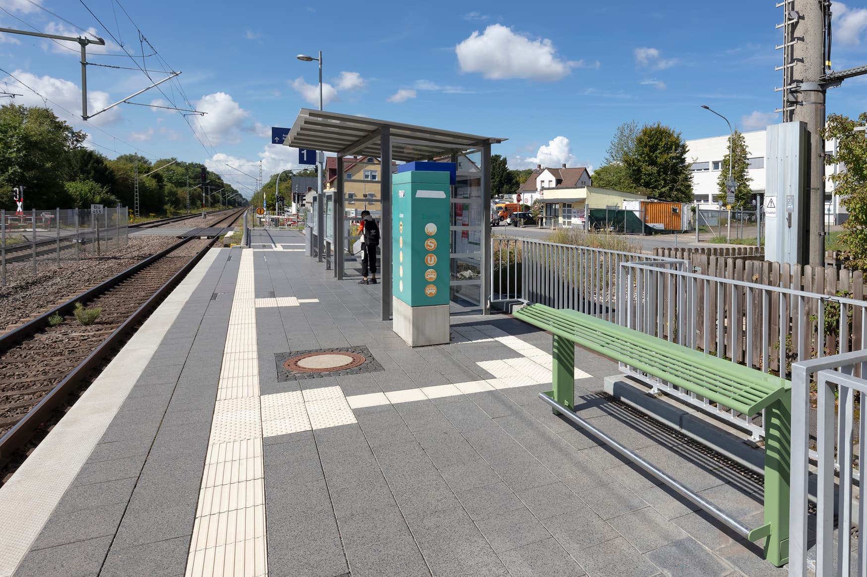 Wetterschutzhäuschen mit Sitzbank. Recht davon neue Anlehner. Dazwischen ein Ticketautomat.