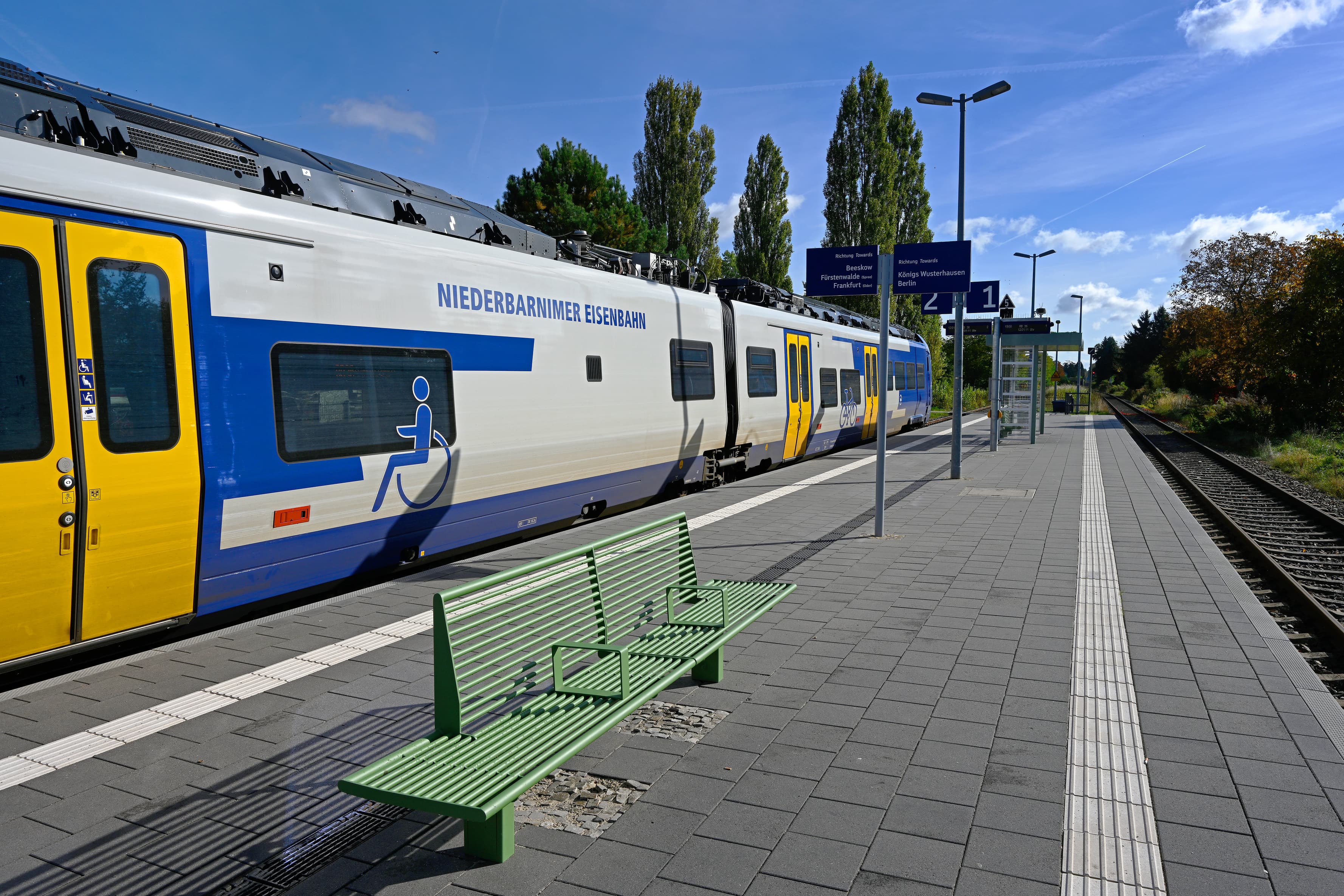 Neue Sitzbänke am Bahnsteig mit eingefahrenem Zug.