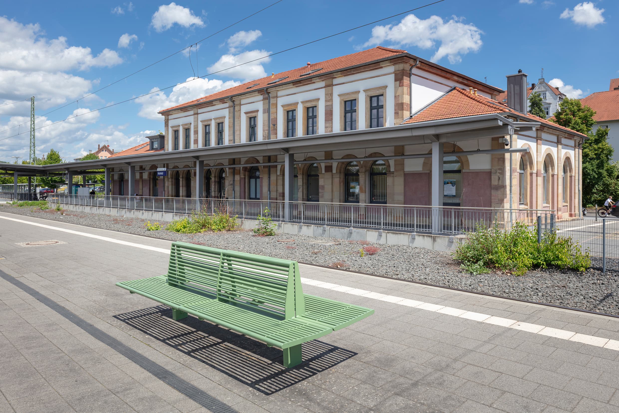 Sanierter Bahnsteig mit neuen Calidum Sitzbänken und dem Empfangsgebäude im Hintergrund am Bahnhof Hünfeld. 