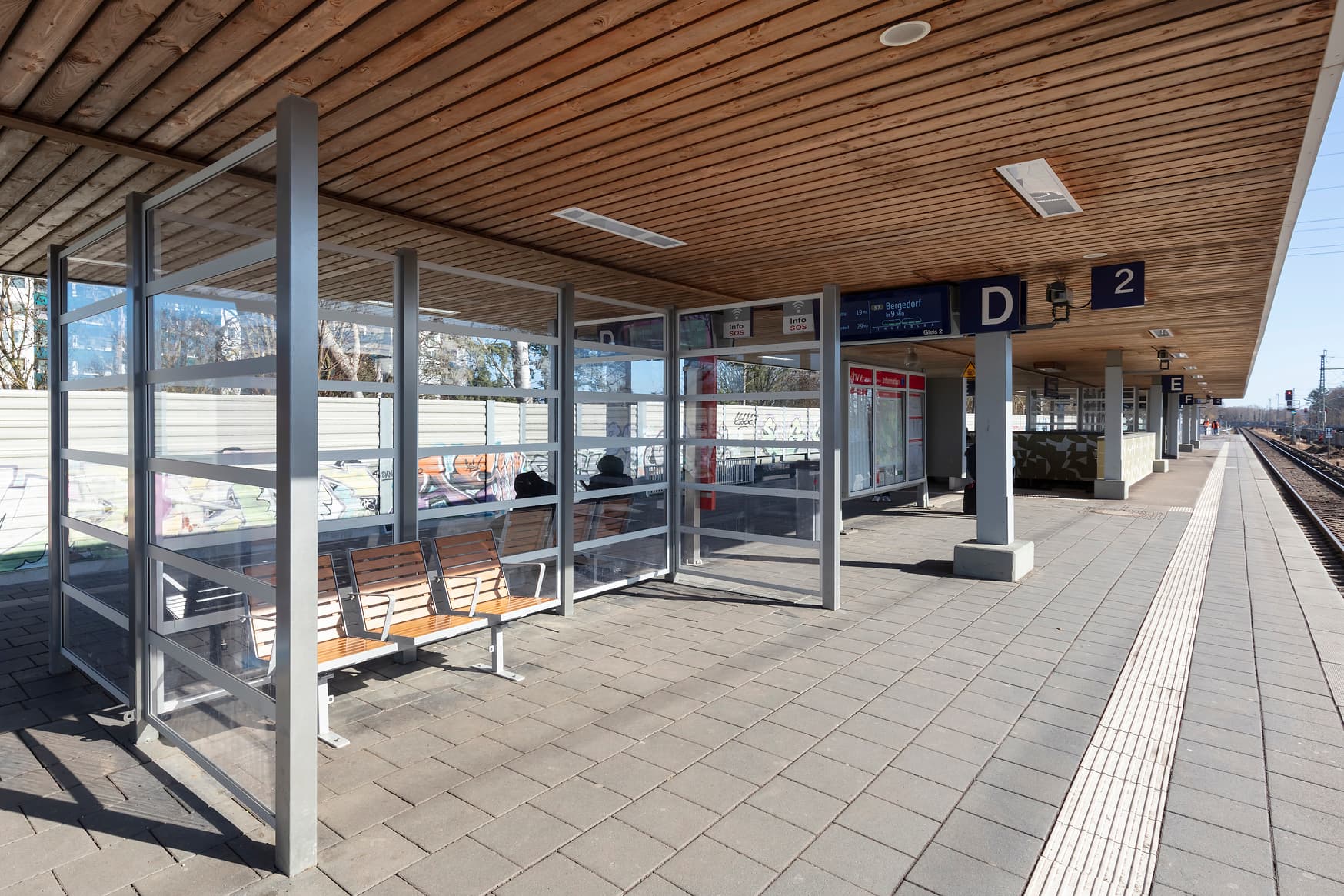 Wetterschutzhaus unter dem Bahnsteigdach mit Sitzbänken.