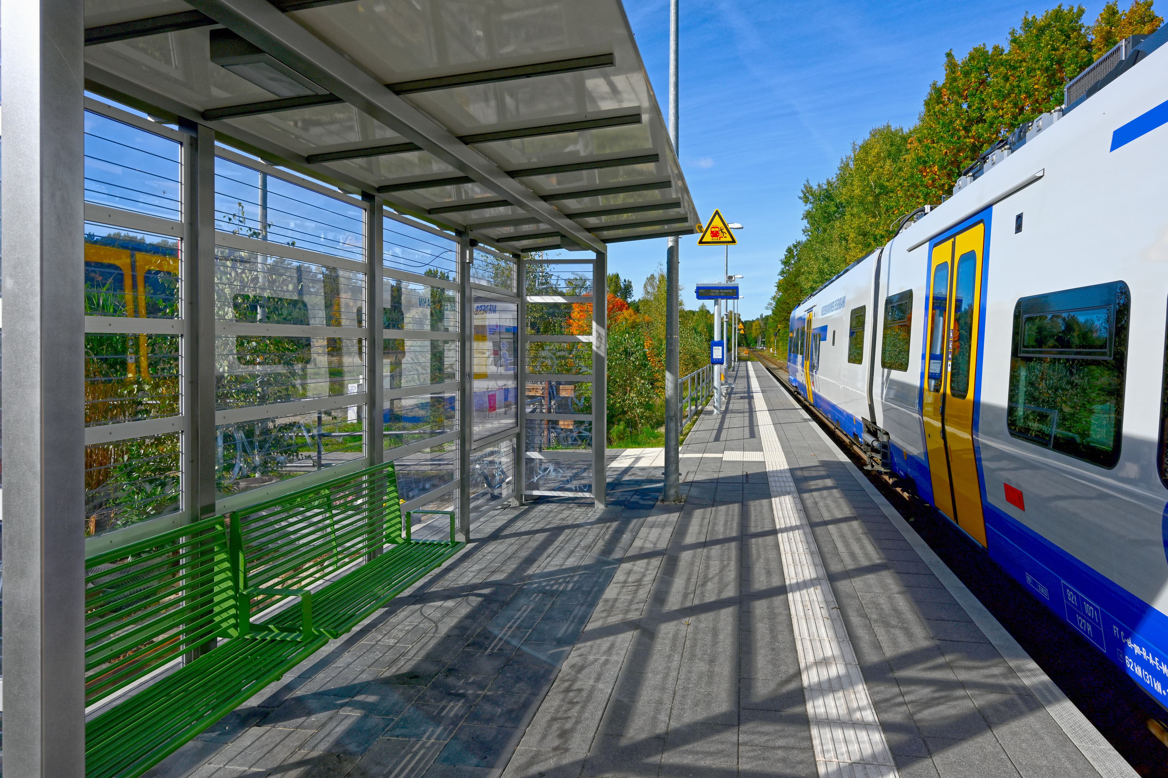 Blick auf ein Wartehaus auf einem Bahnsteig links, ein haltender Zug rechts. 