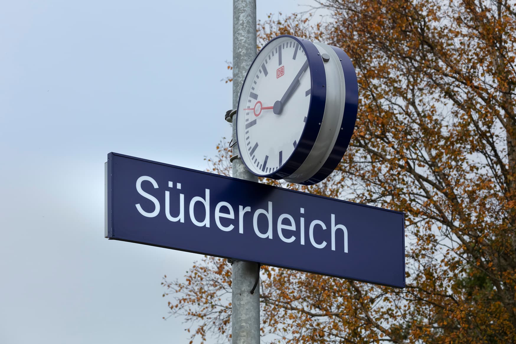 Blaues Bahnhofsschild Süderdeich an einer Stele darüber die Bahnhofsuhr.