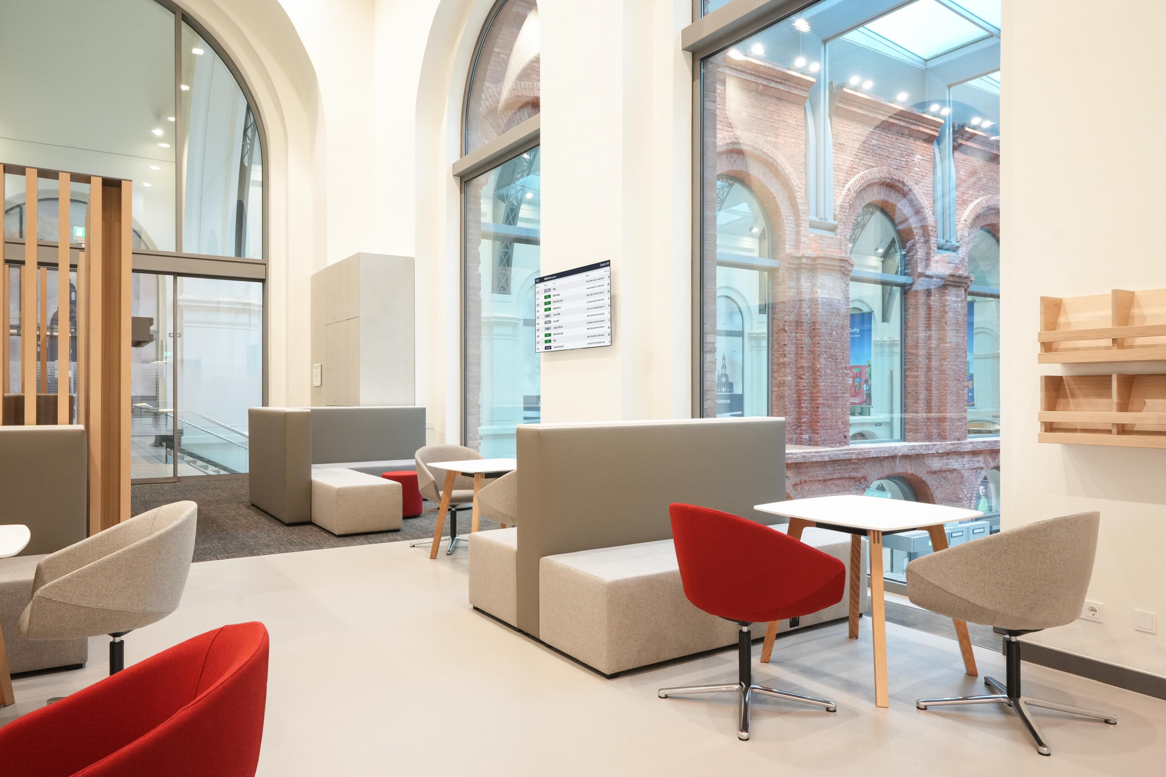 Graue und rote Rundstühle definieren zusammen mit kleinen weißen Tischen und Sitzbänken verschiedene Sitzbereiche.
