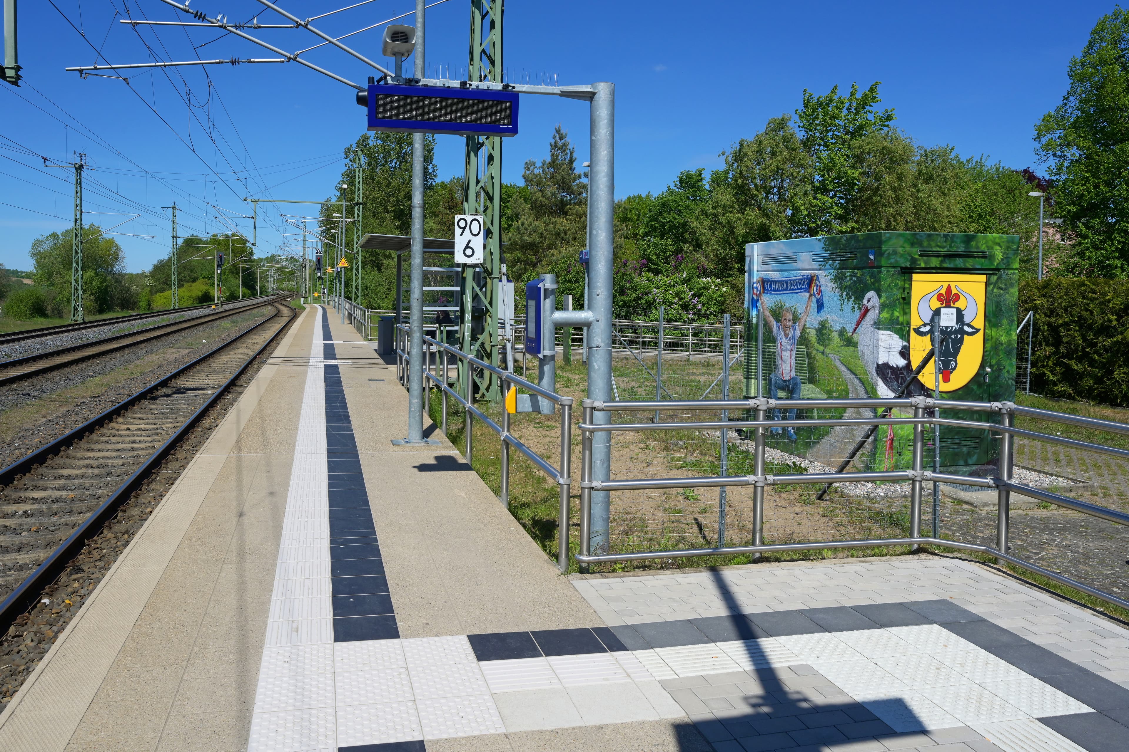 Bahnsteig mit Wetterschutzhäschen und neuem Geländer. Im rechten Bildrand ein Häuschen mit bemalter Wand.
